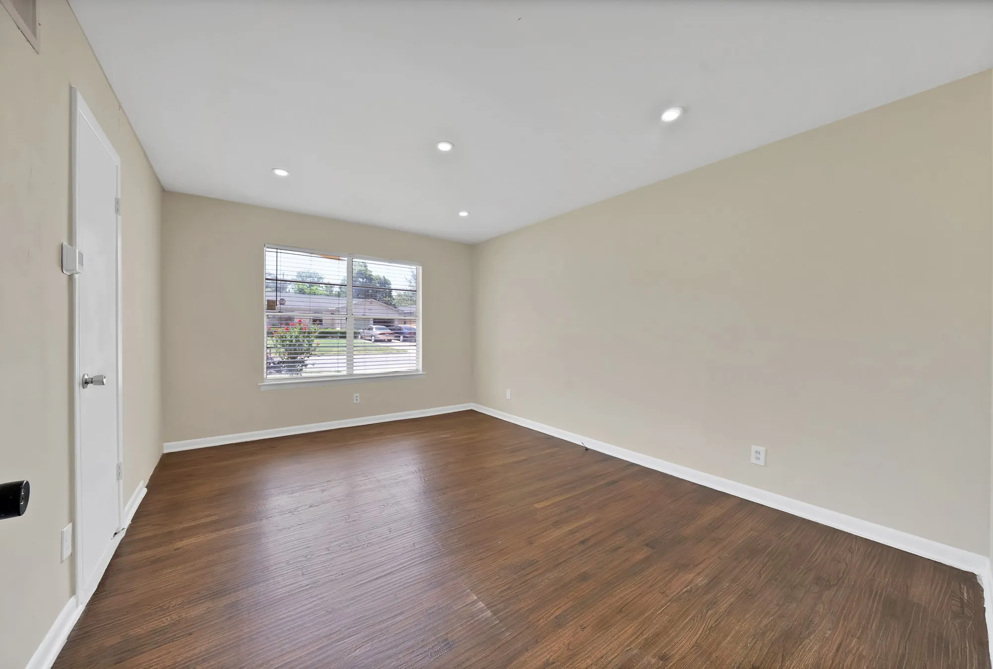 Living space featuring wood-finish flooring, neutral wall tones, recessed ceiling lighting, and a large window with horizontal blinds