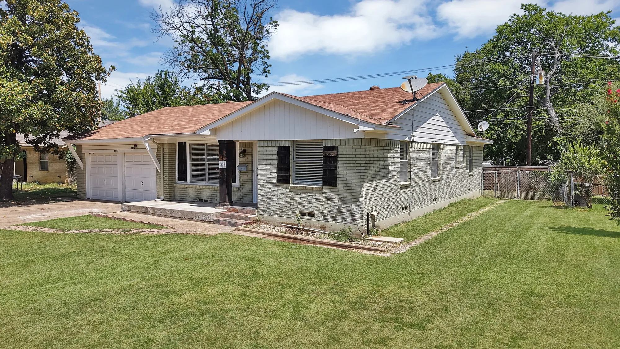 Ranch-style residence featuring a brick facade with light-colored paint, a brown shingle roof, and a two-car garage
