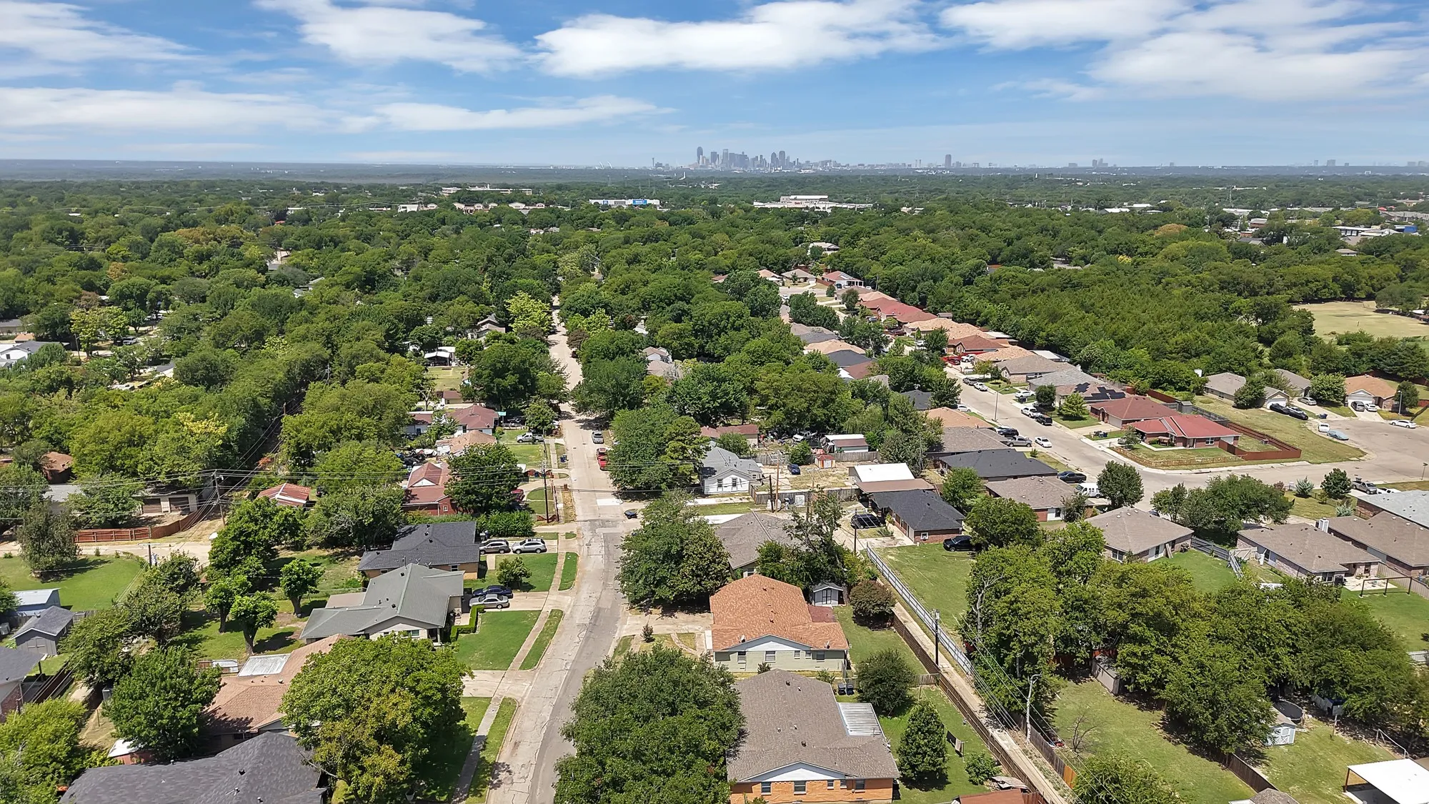 Expansive residential area featuring numerous single-story homes, mature tree coverage, and a distant city skyline