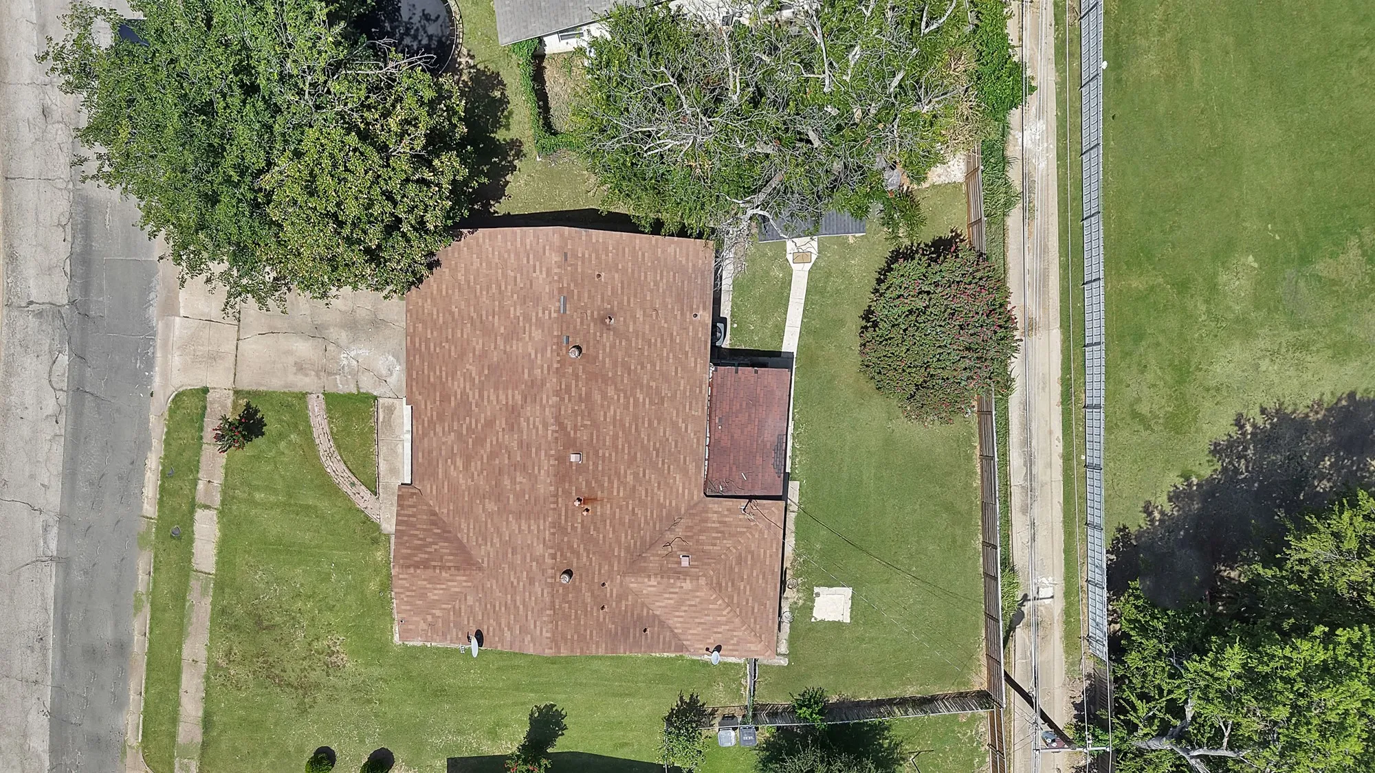 Property featuring a brown shingle roof, concrete driveway, and front lawn with mature trees