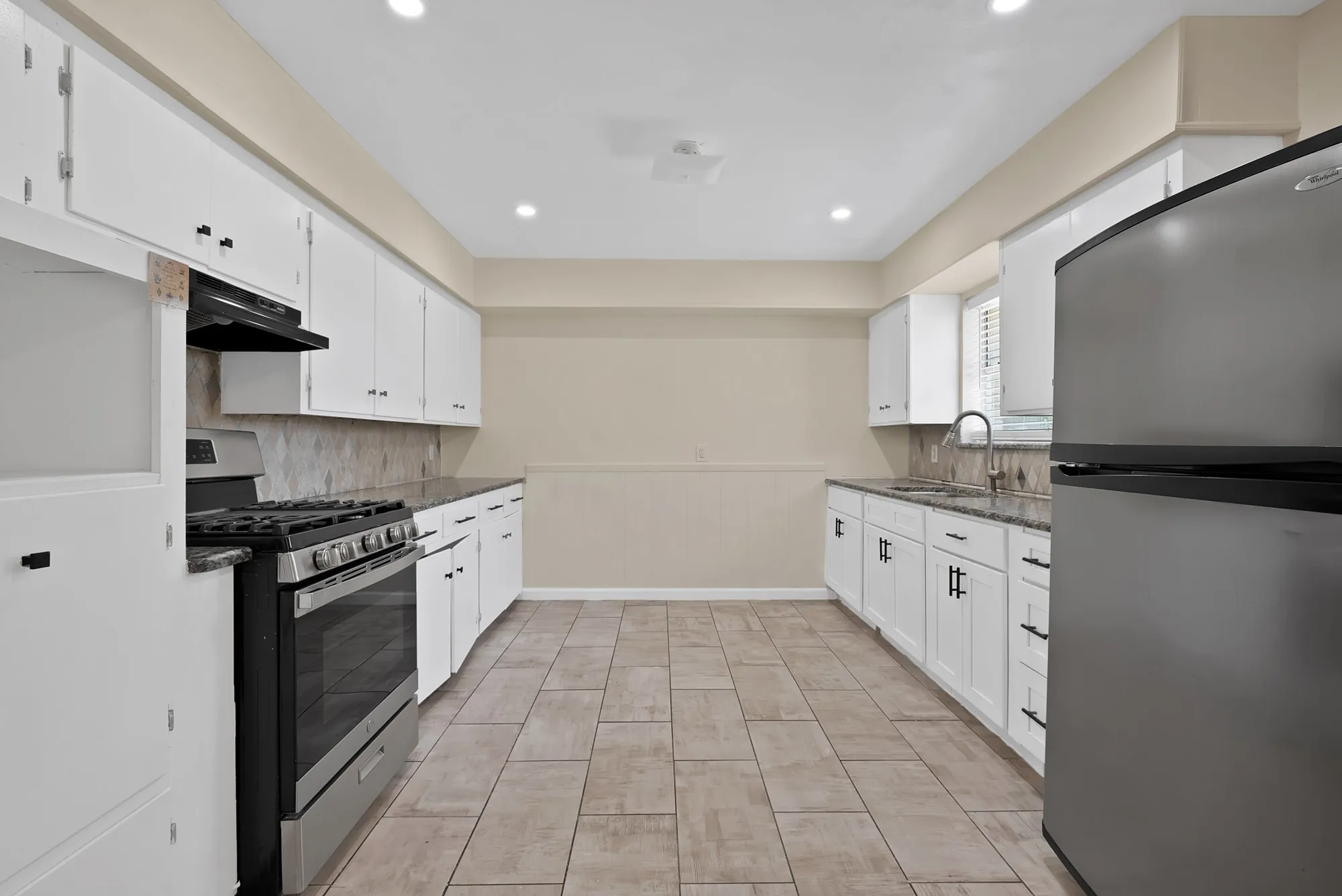 Kitchen featuring stainless steel appliances, white cabinetry with dark hardware, granite countertops, tile backsplash, and recessed lighting
