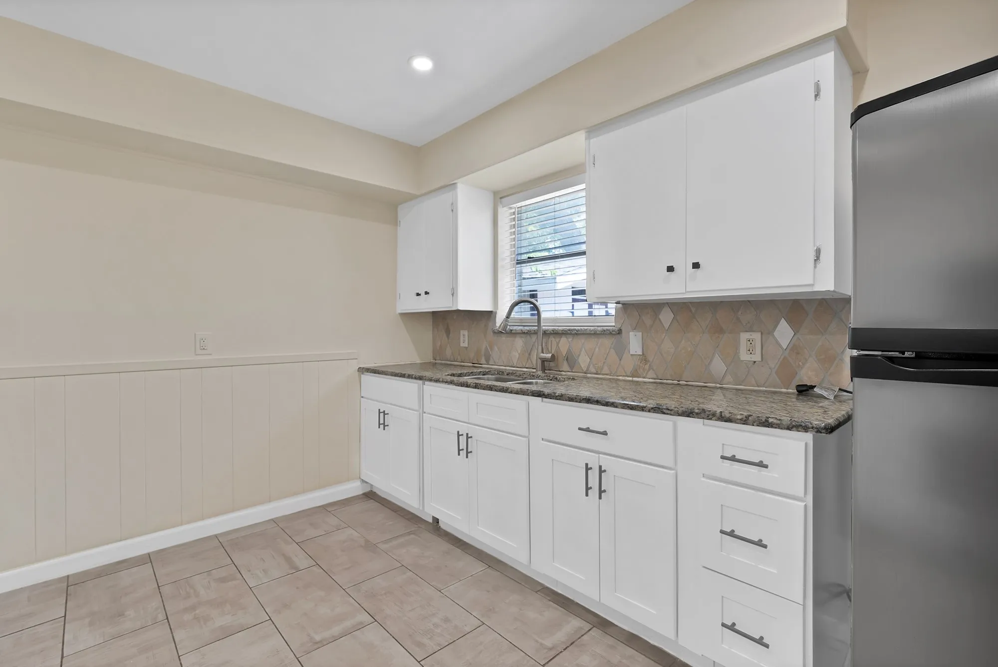 Kitchen featuring white cabinetry, a stainless steel refrigerator, granite countertops, a tile backsplash, and tile flooring