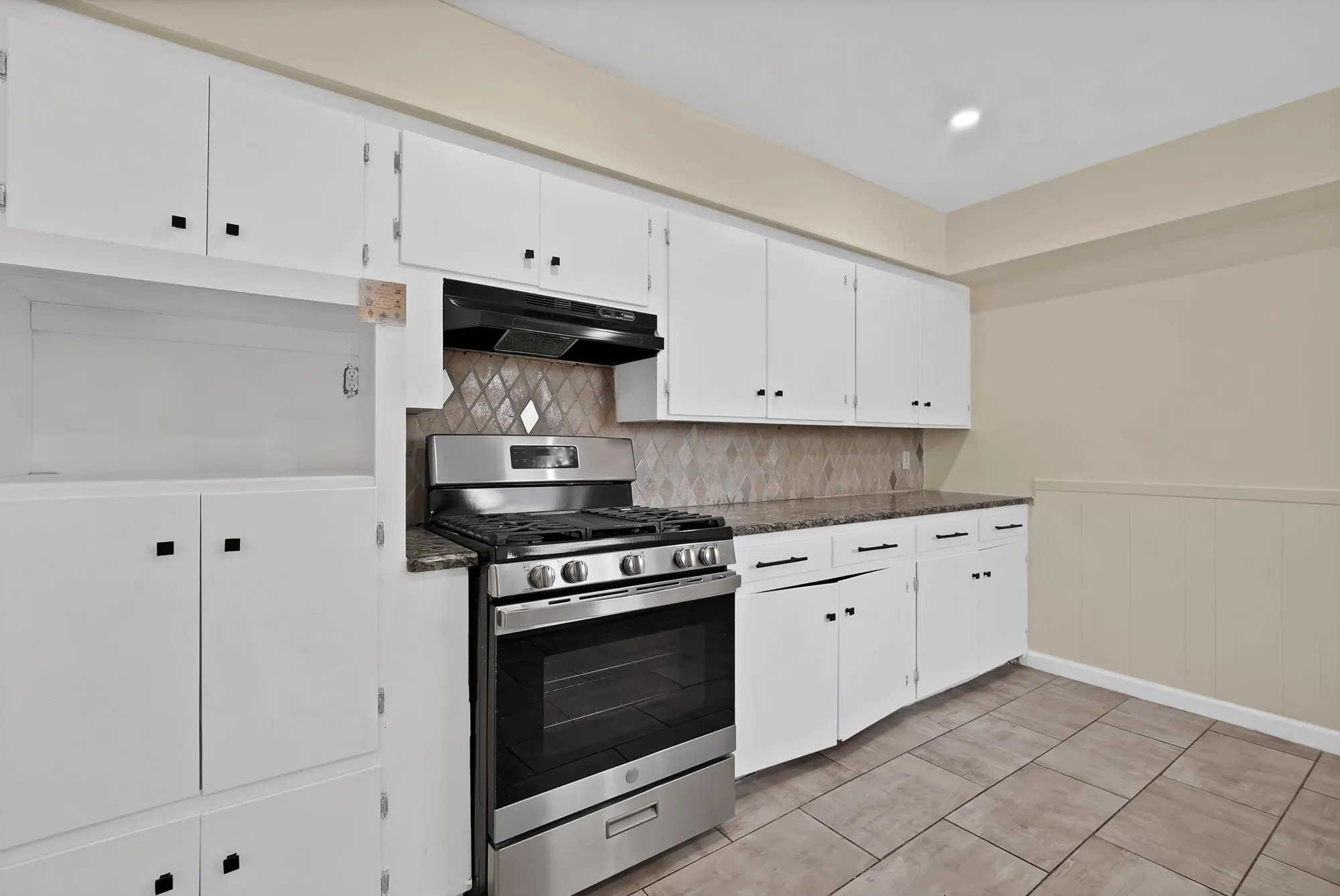 Kitchen featuring a stainless steel range with overhead ventilation, white cabinetry, granite-finish countertops, and a diamond-patterned tile backsplash