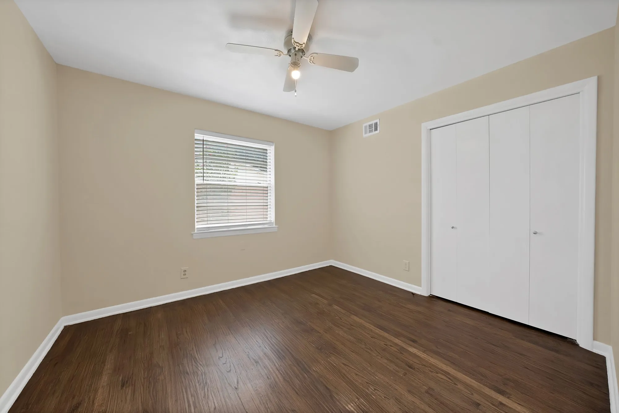 Bedroom featuring wood-finish flooring, neutral wall tones, a ceiling fan with integrated lighting, a window with horizontal blinds, and a bi-fold closet
