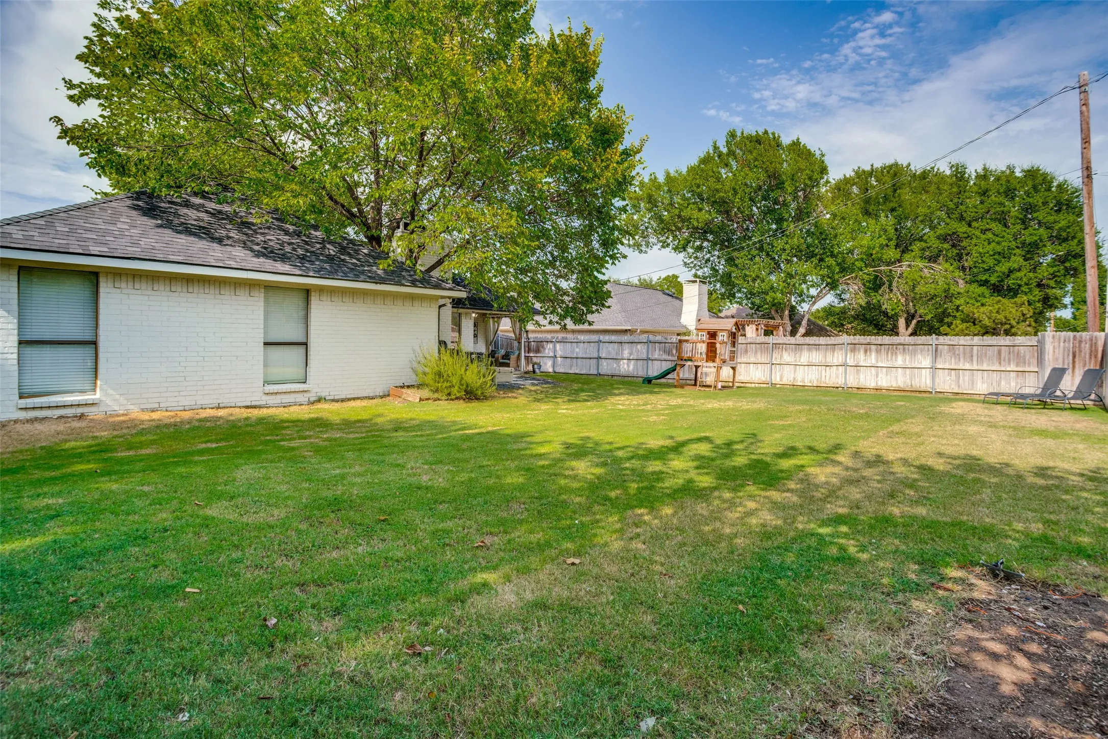 Spacious backyard with a wooden privacy fence, mature trees, and a substantial grassy area