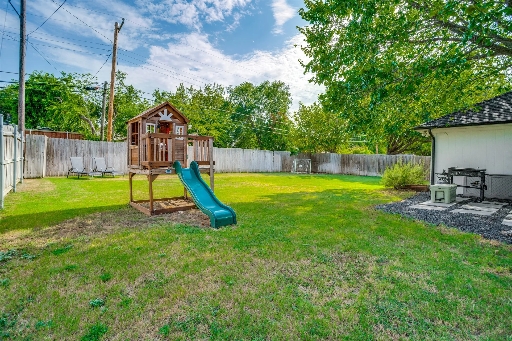 Expansive backyard featuring a lush lawn, wooden privacy fencing, mature trees, and a dedicated patio area with paver stones and decorative gravel