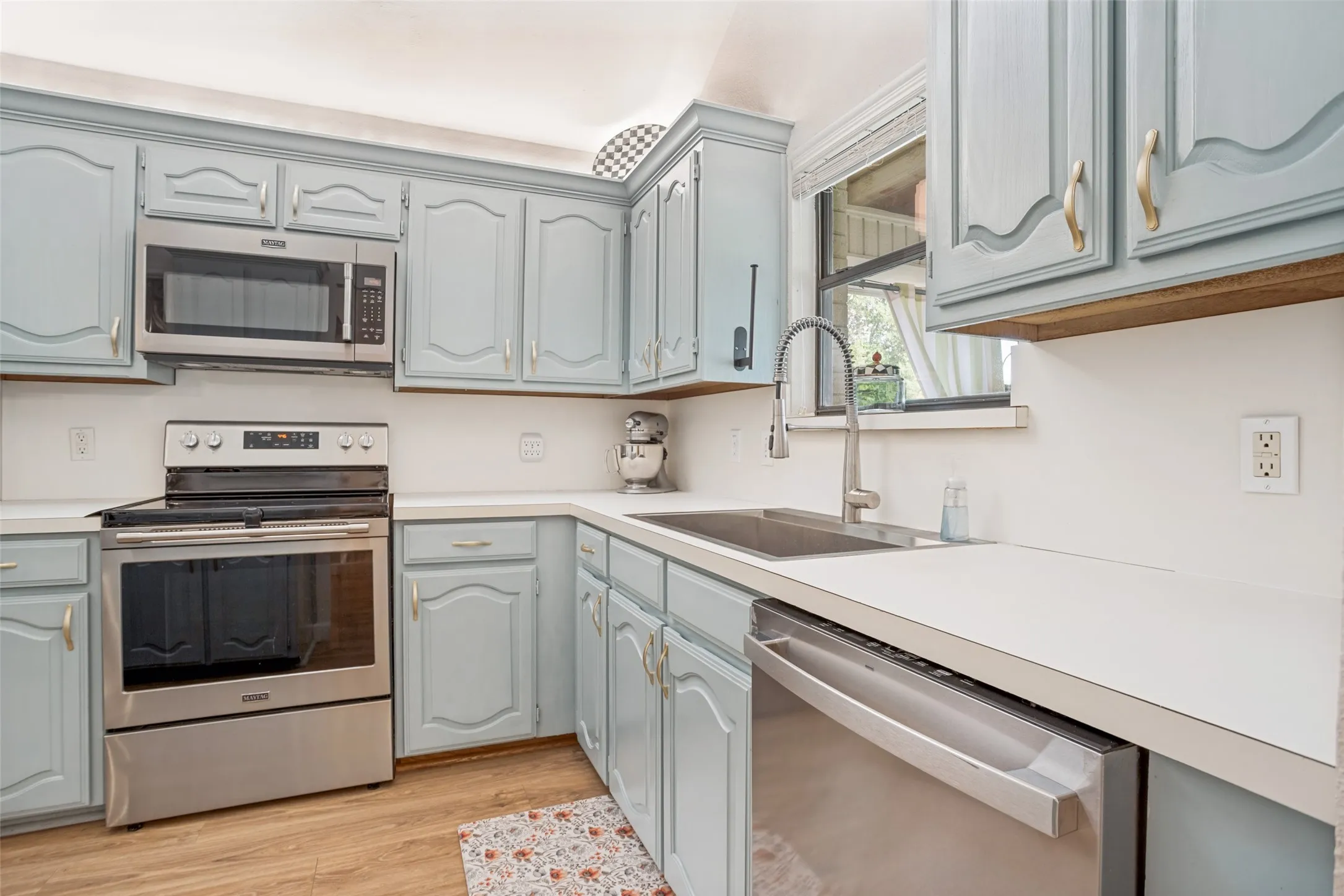 Updated kitchen featuring light blue cabinetry with arched door details, stainless steel appliances including a slide-in range and dishwasher, undermount sink with gooseneck faucet, quartz countertops, wood-finish flooring, and ample storage with open shelving above the counter
