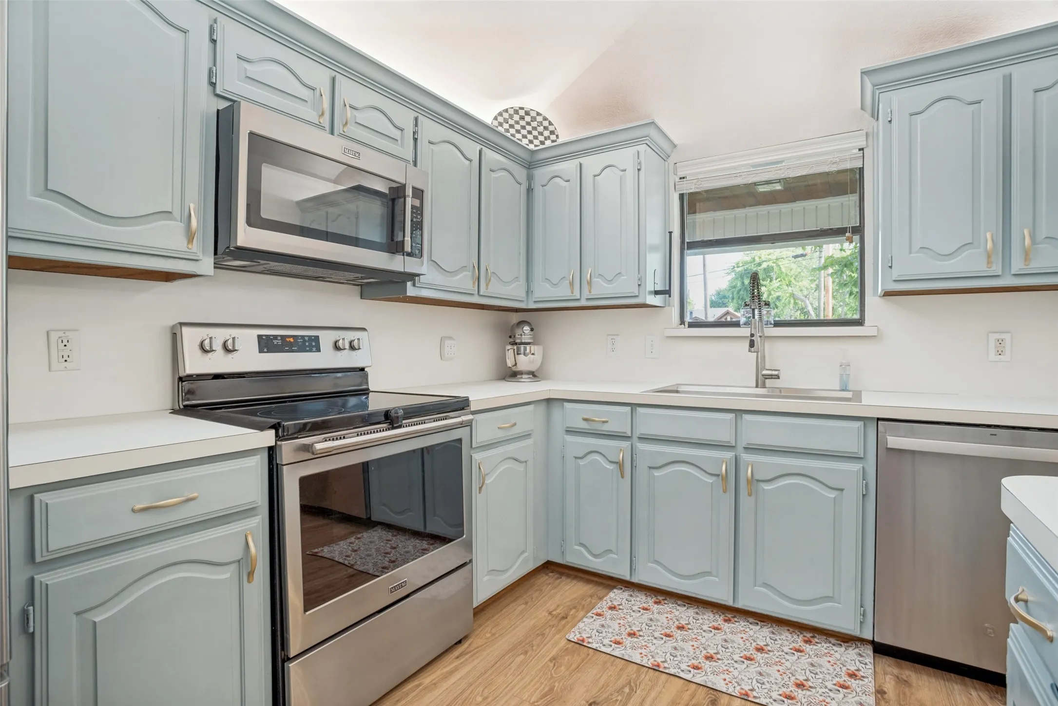 Kitchen featuring light blue cabinetry with gold-toned hardware, white countertops, and wood-finish flooring
