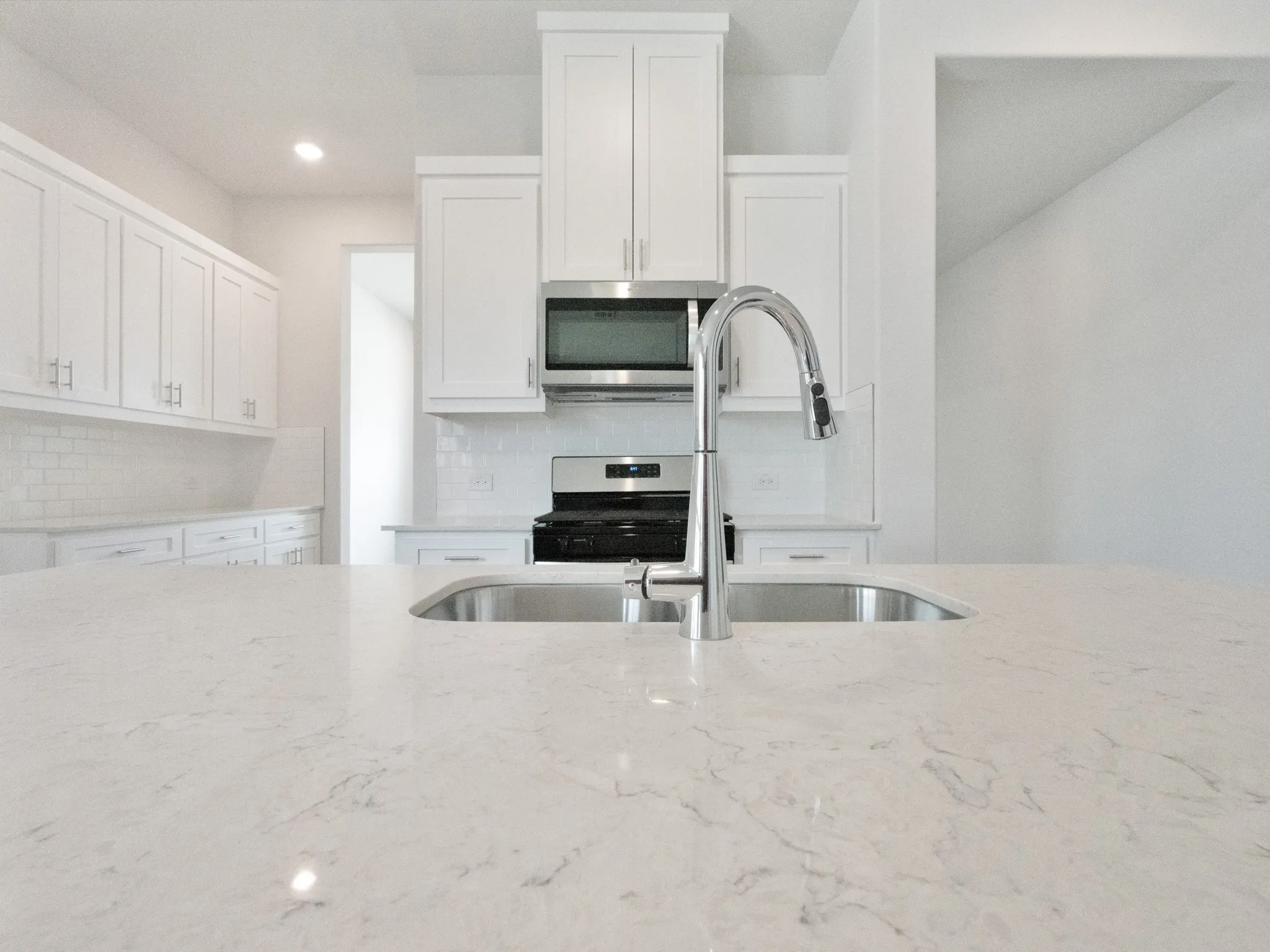 Kitchen featuring white cabinets, stainless steel appliances, backsplash, light stone countertops, and recessed lighting