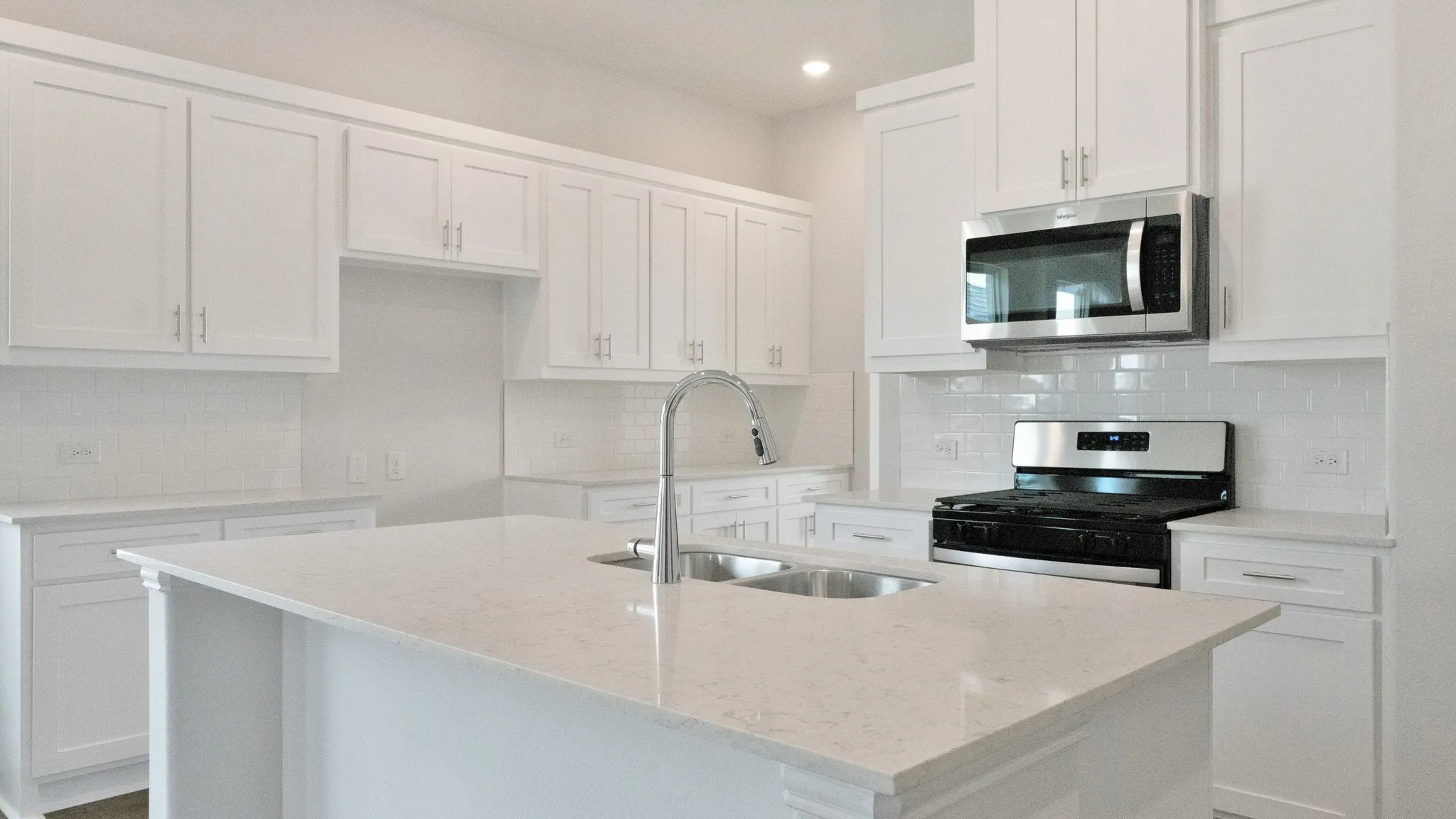 Kitchen with white cabinets, appliances with stainless steel finishes, tasteful backsplash, a kitchen island with sink, and light stone counters