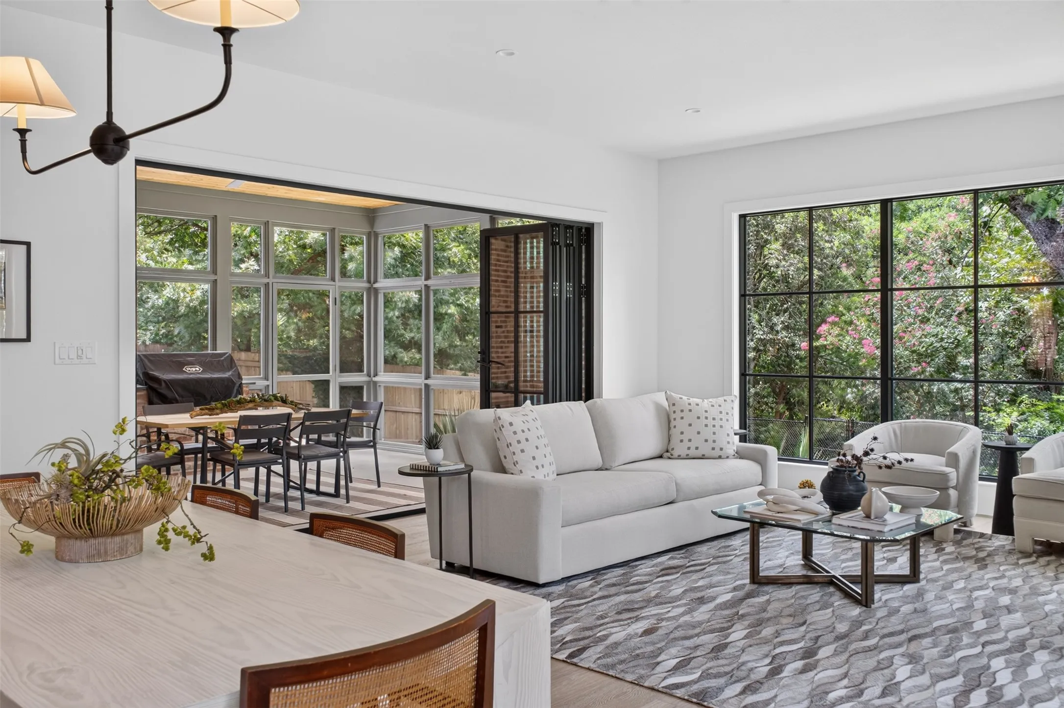 Bright living area featuring expansive grid-pattern windows, a retractable glass wall, wood-finish flooring, and a contemporary chandelier