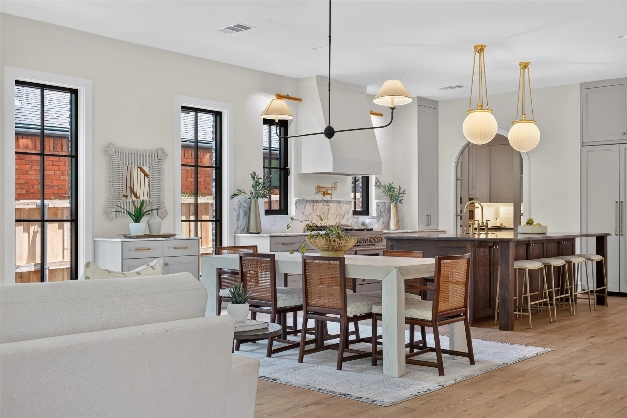 Open-concept living space featuring wood-finish flooring, a kitchen island with seating, a built-in range hood, and multiple windows with black framing