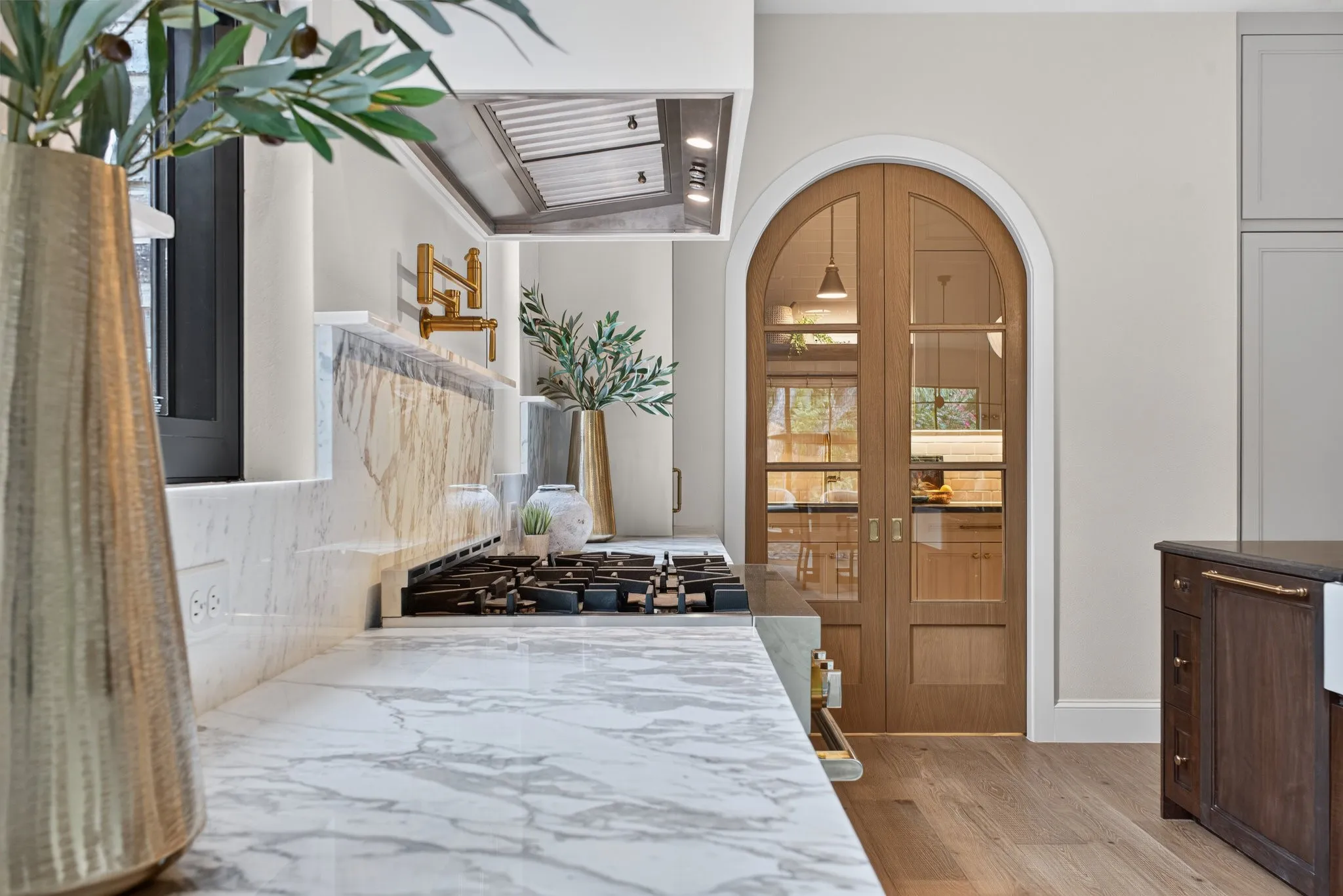 Gourmet kitchen featuring a built-in gas range, marble countertops and backsplash, a stainless steel range hood, and a gold-tone wall-mounted pot filler