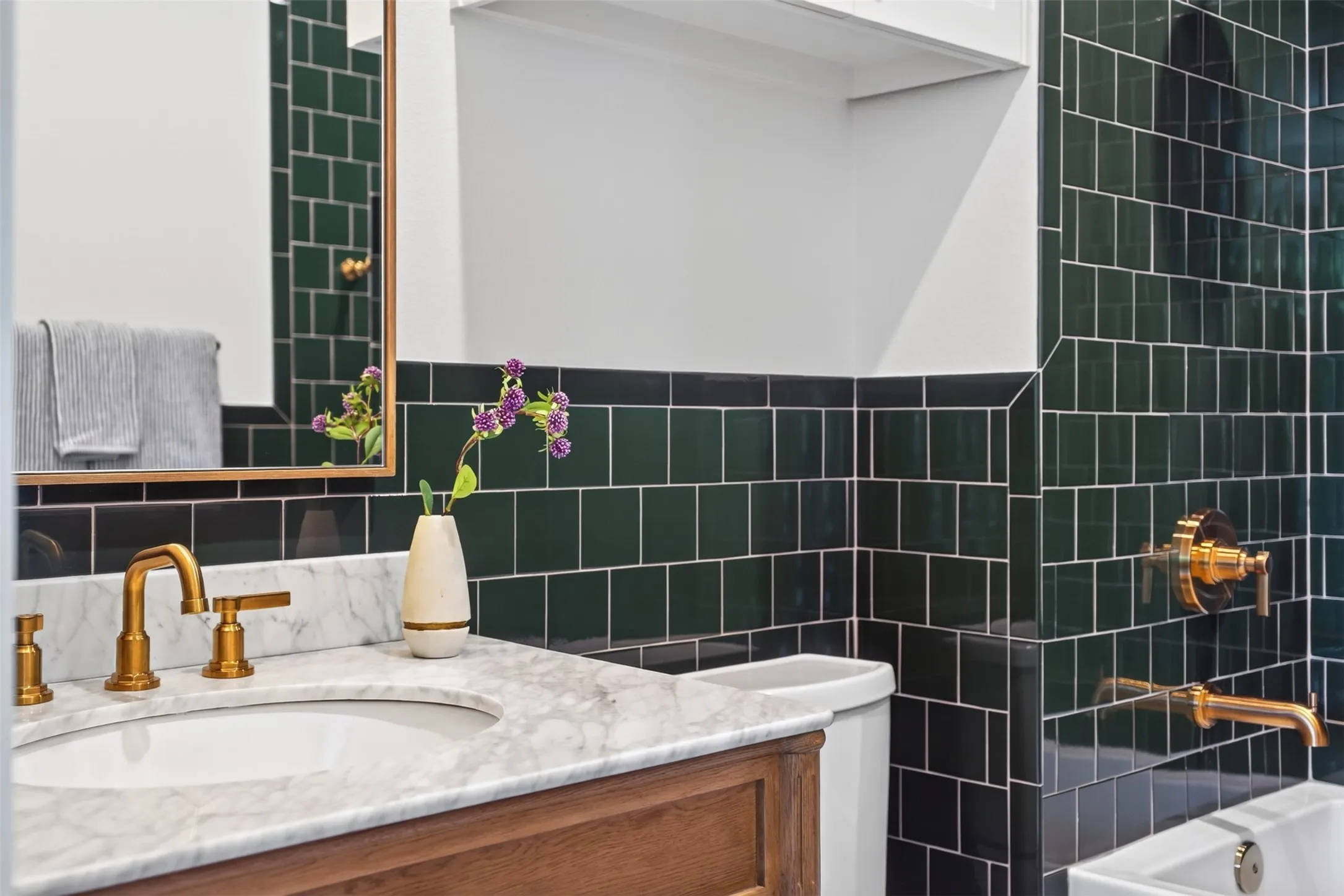 Bathroom featuring dark green subway tile, a marble-finish countertop, and gold-tone fixtures