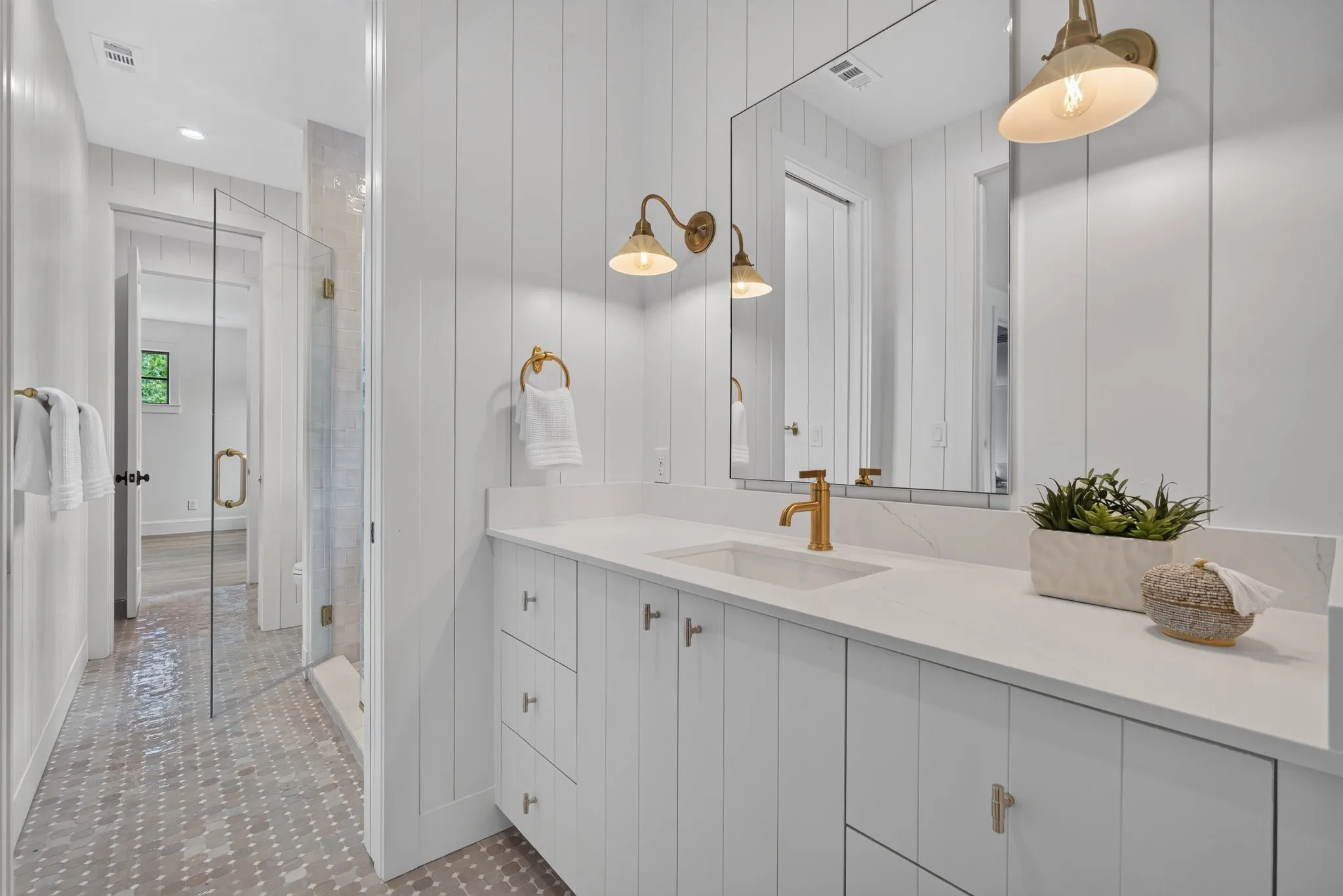 Bathroom featuring a white vertical shiplap wall, a white vanity with gold hardware, a rectangular undermount sink with a gold faucet, a large frameless mirror, and hexagonal tile flooring
