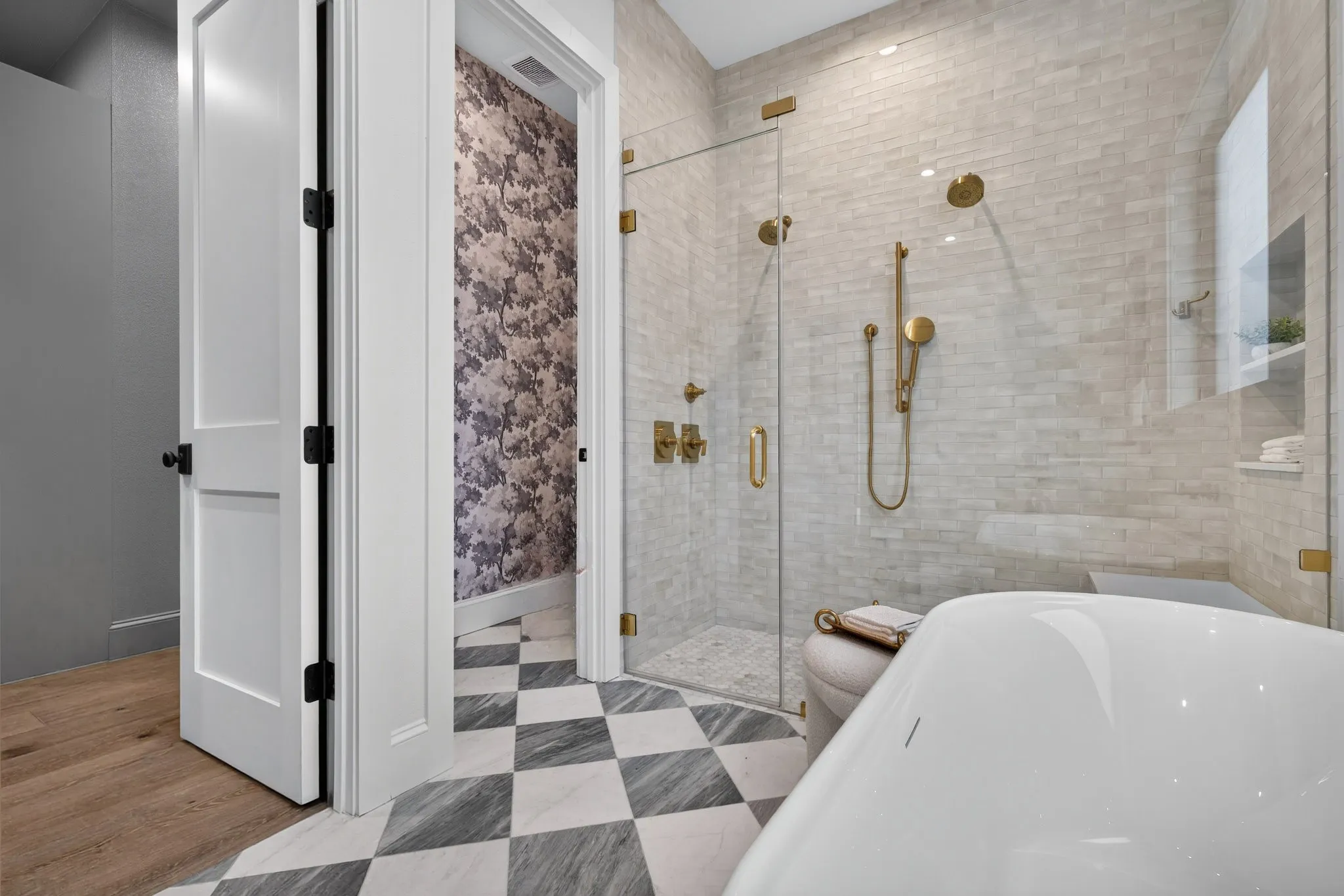 Bathroom featuring a walk-in glass shower enclosure with brass fixtures, light-toned subway tile, a freestanding soaking tub, and checkerboard floor tiling