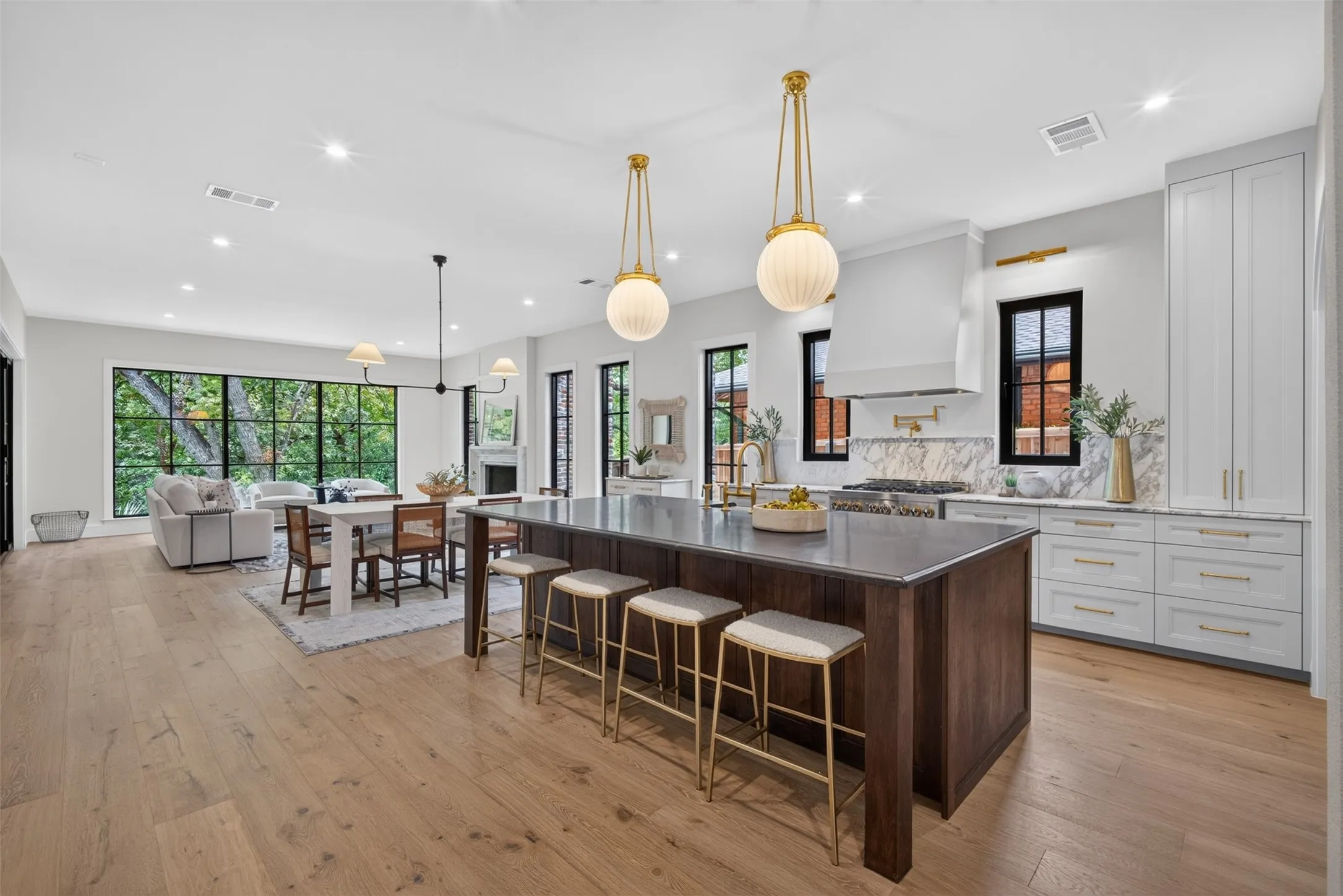 Gourmet kitchen featuring a large central island, white cabinetry, integrated range hood, and light wood-finish flooring