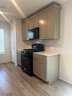 Kitchen featuring shaker-style cabinetry, black appliances, tile backsplash, and wood-finish flooring