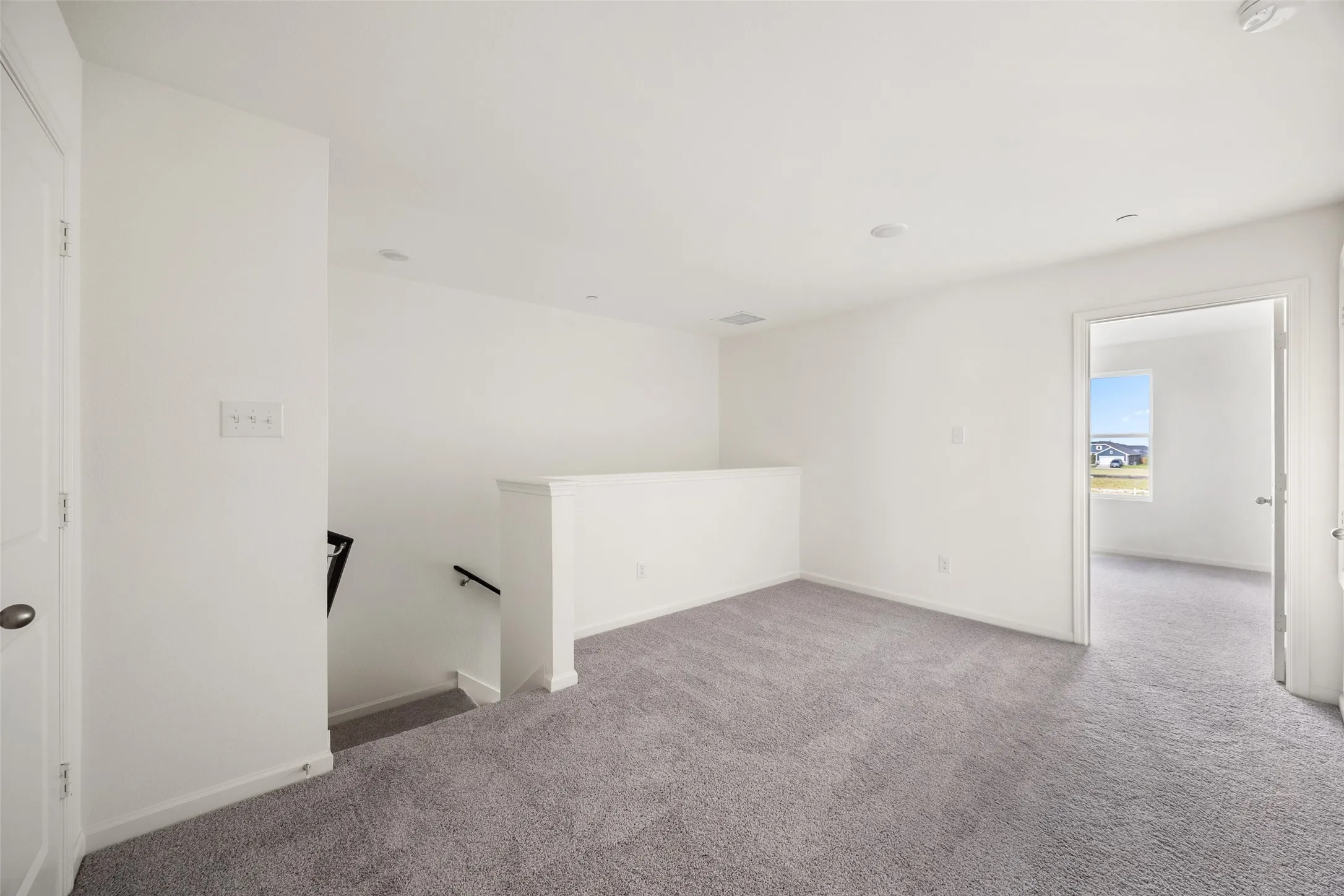 Upper-level landing featuring light gray carpeting, white walls, recessed lighting, and a white banister