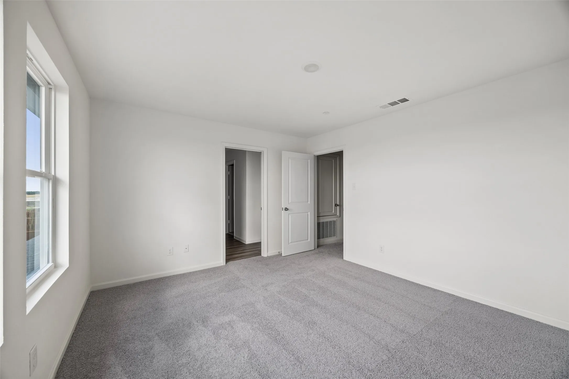 Spacious room with plush gray carpeting, white painted walls, and a large window