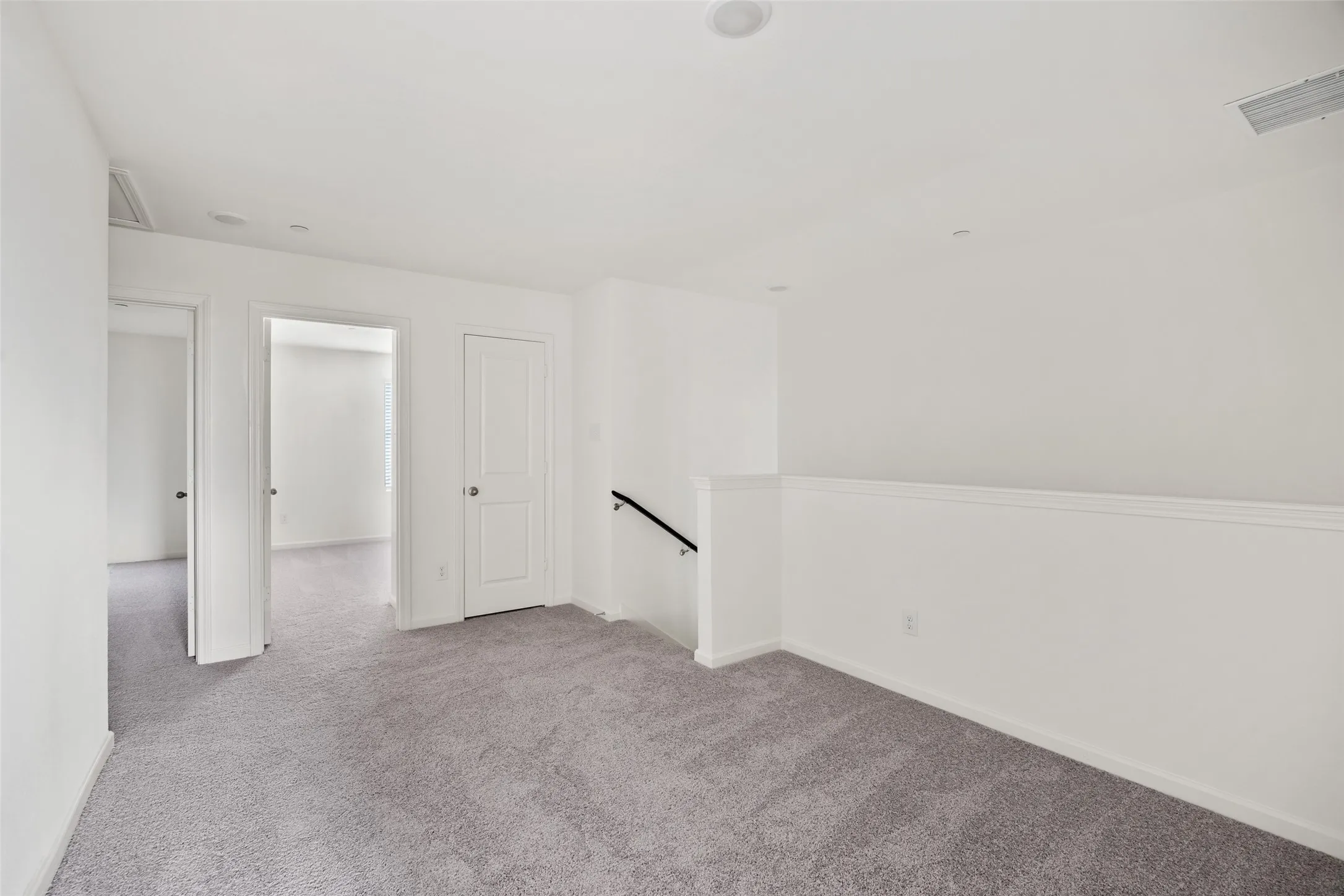 Open landing area featuring light gray carpet, crisp white walls, recessed lighting, and a white balustrade with a black handrail