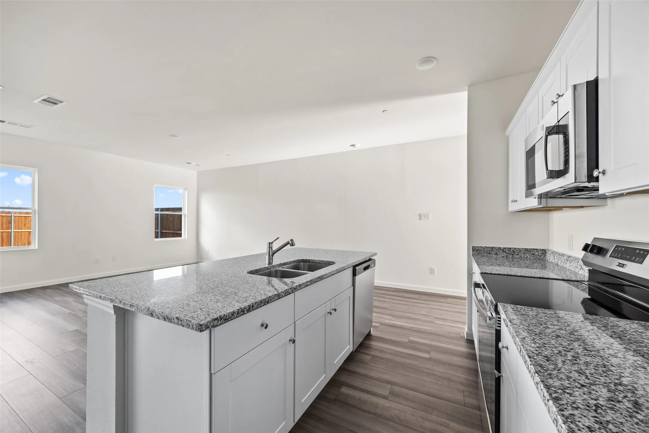 Modern kitchen featuring an island with a double basin sink, granite countertops, wood-finish flooring, white cabinetry, and stainless steel appliances
