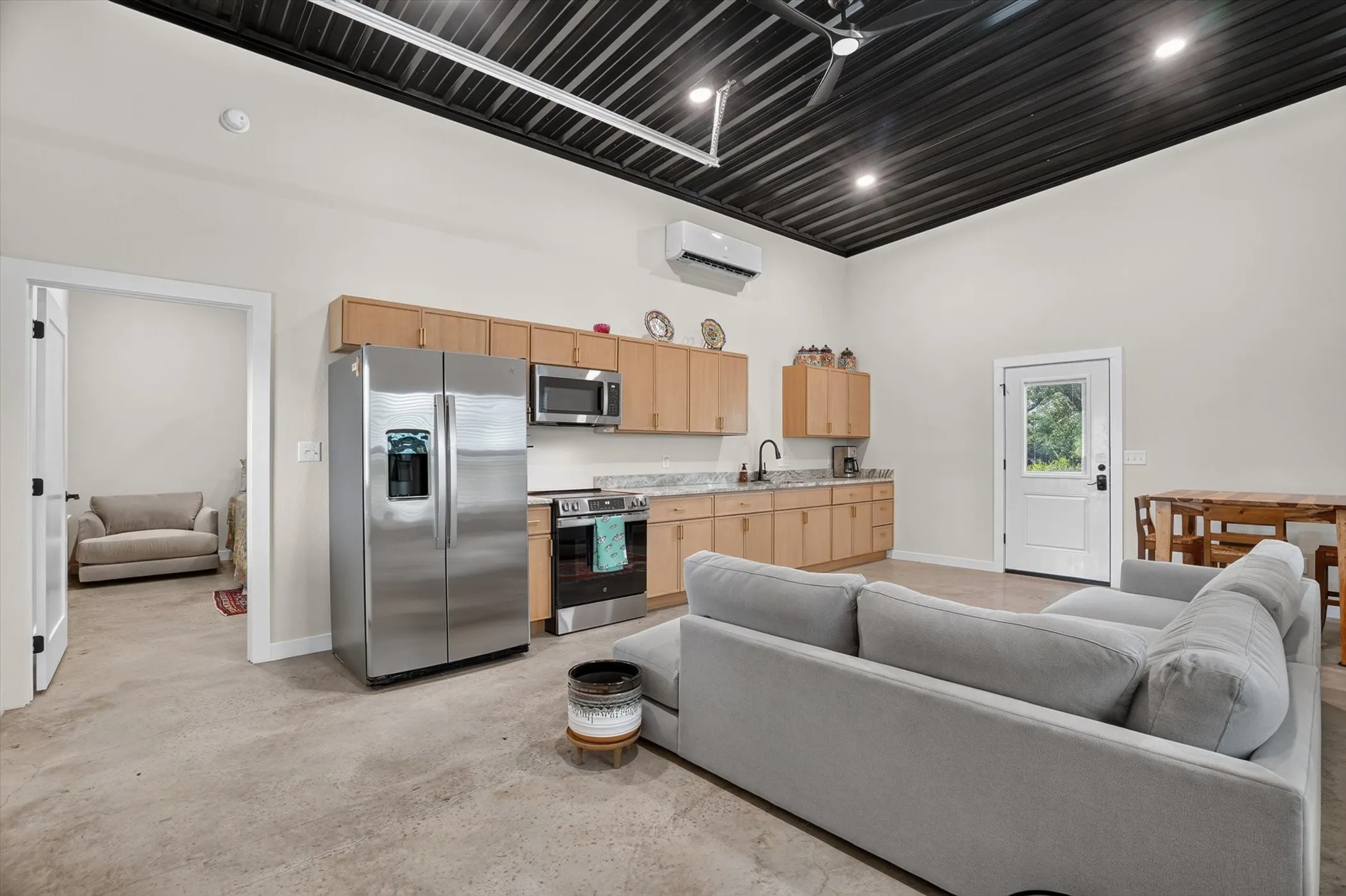 Open-concept living space featuring a full kitchen with stainless steel appliances, light wood-finish cabinetry, and light-toned countertops