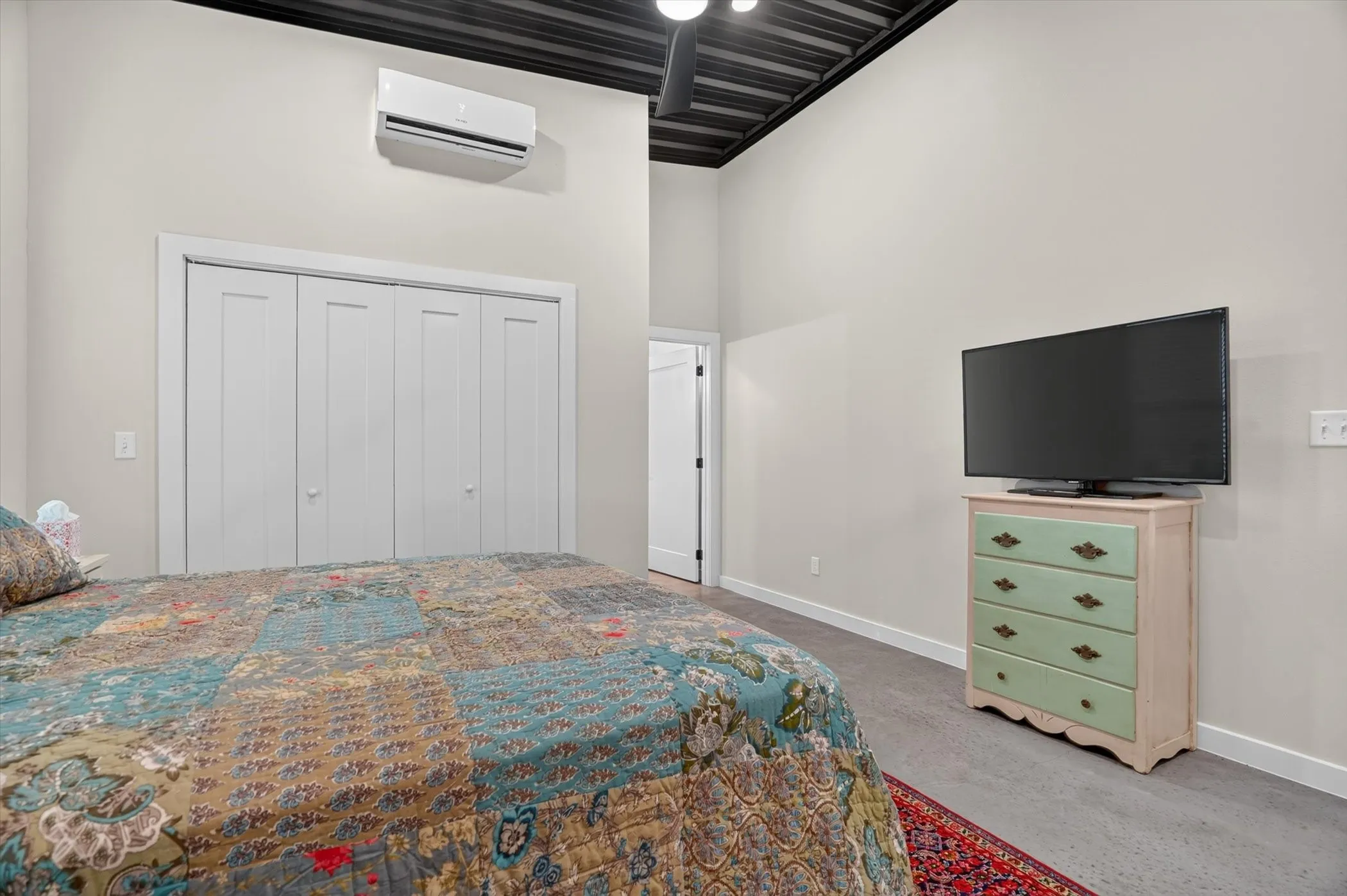 Carpeted room featuring a ceiling-mounted mini-split HVAC unit, bi-fold closet doors, and exposed ceiling joists