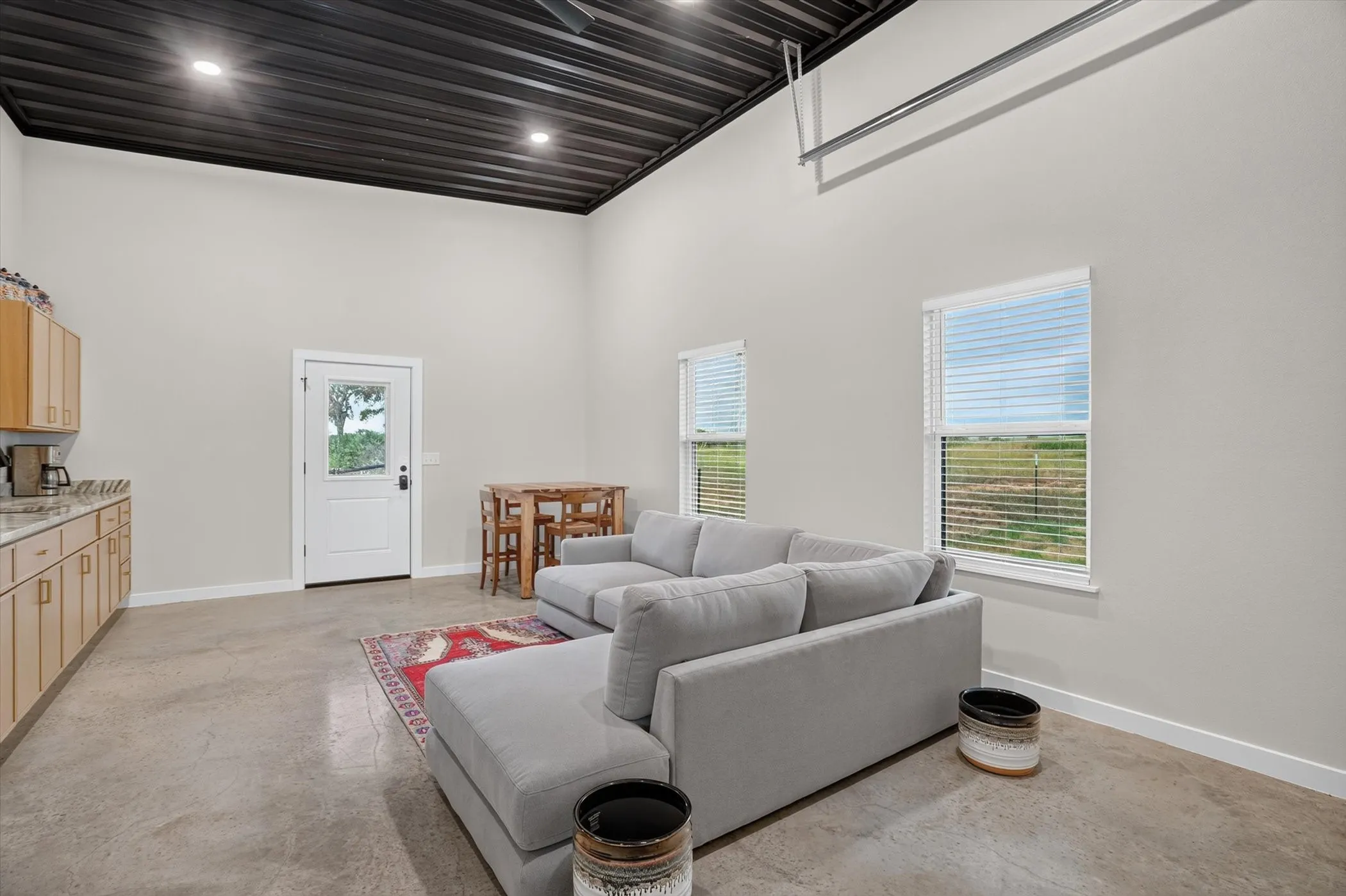Spacious living area featuring high ceilings with exposed black corrugated metal, recessed lighting, and polished concrete flooring