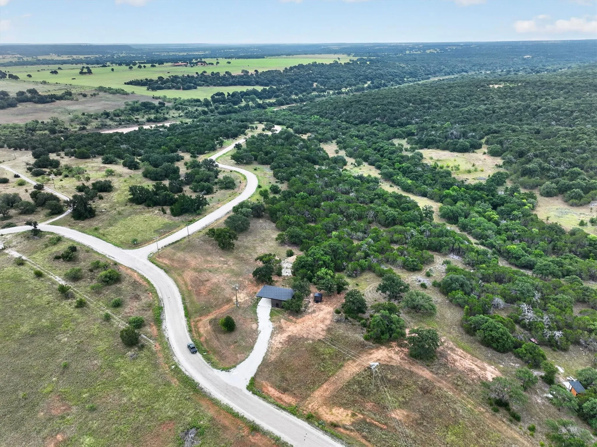 Expansive rural landscape featuring a winding road network, abundant mature trees, open grassy areas, and a distant tree line