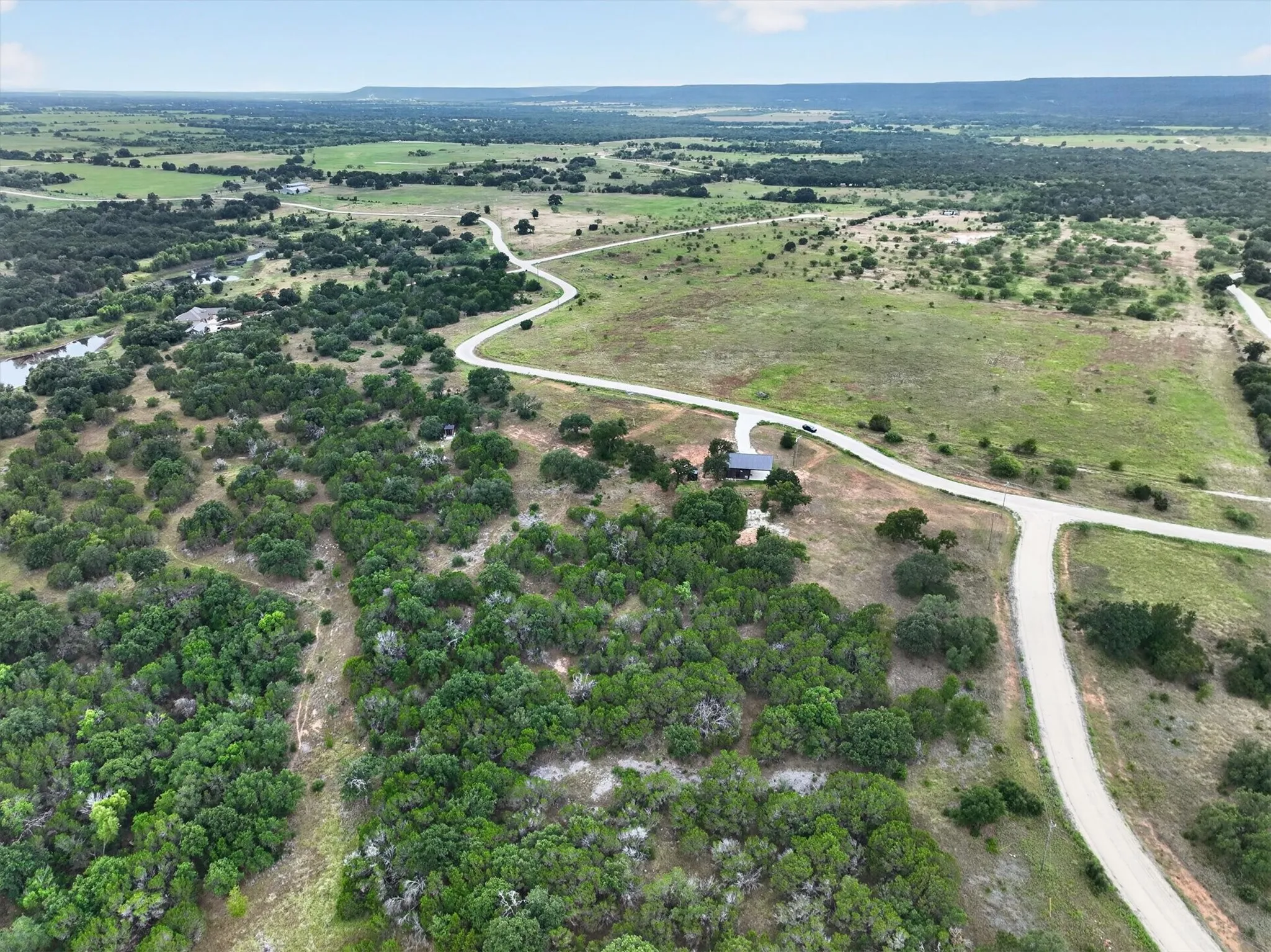 Expansive rural landscape featuring winding roads, scattered mature trees, and distant hills