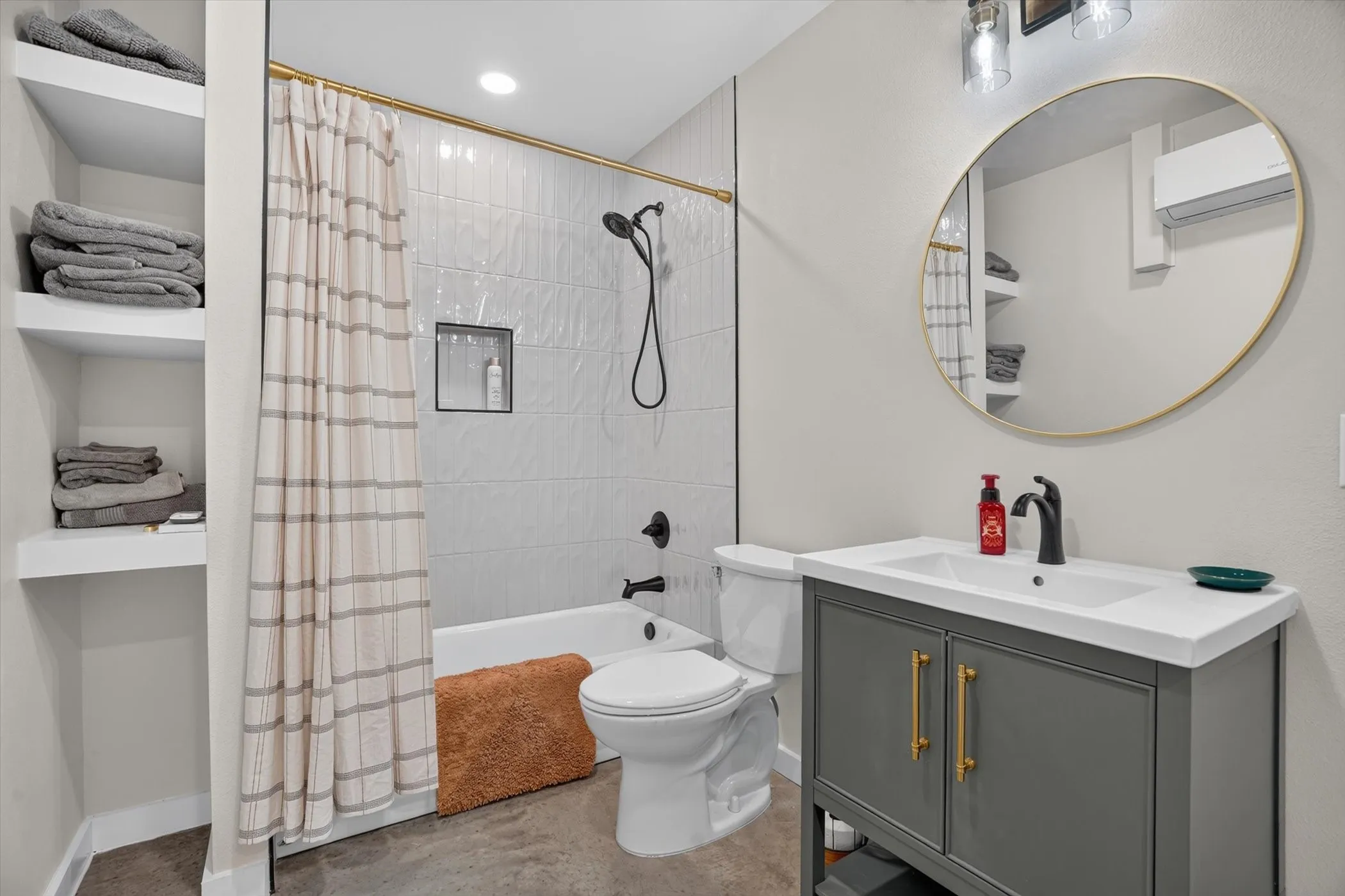 Bathroom featuring a white bathtub with dark fixtures, light-toned tiled shower surround with a recessed niche, and an integrated ceiling light