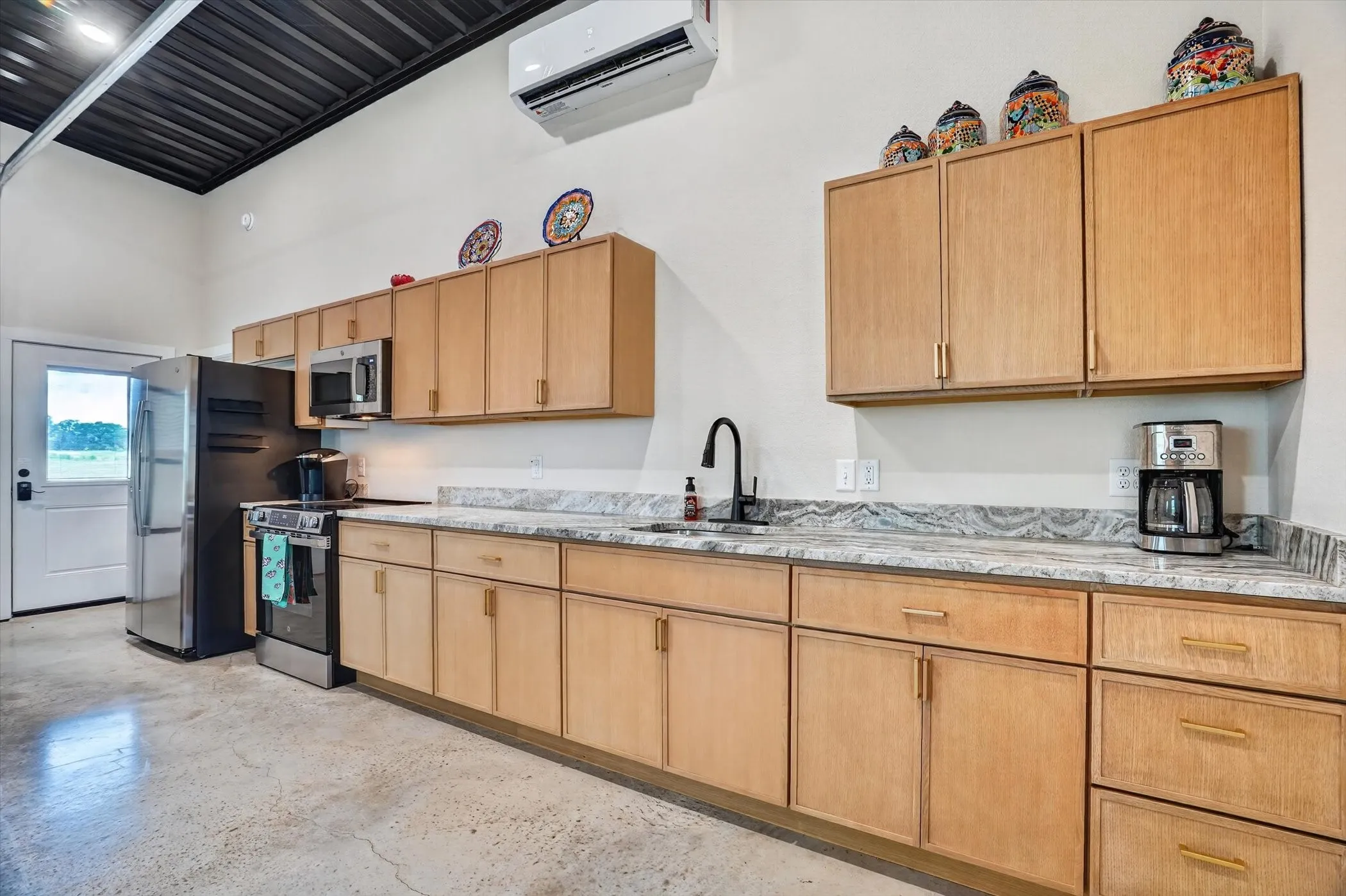 Full kitchen featuring light wood cabinetry, stainless steel appliances, a black faucet, and patterned countertops