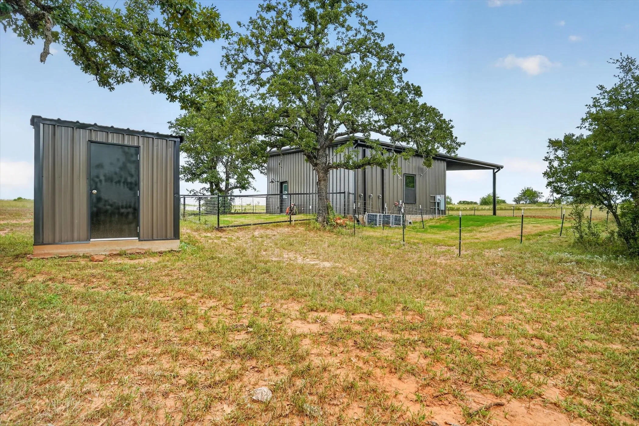 Metal-sided outbuilding with black door, accompanied by a main structure featuring a covered patio and vertical windows