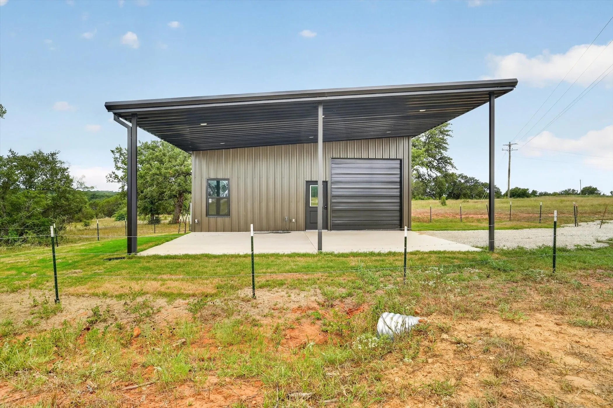 Modern metal building featuring a cantilevered carport, a roll-up garage door, an exterior door, and a single window