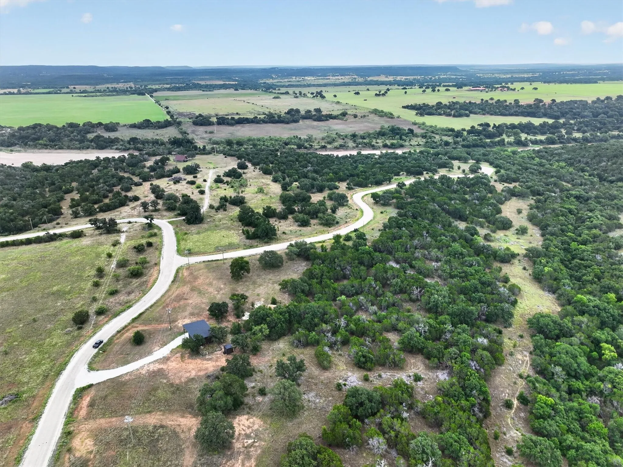 Expansive rural landscape featuring a winding paved road, numerous mature trees, and natural vegetation