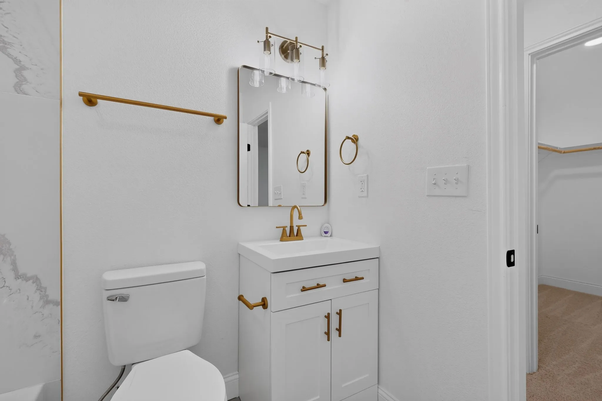 Bathroom featuring a white vanity with gold-tone hardware, a rectangular mirror, and a three-light vanity fixture