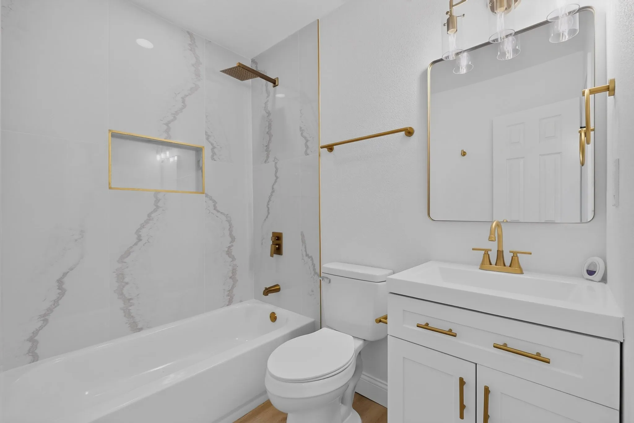 Bathroom featuring a shower-tub combination with a recessed niche, gold-finish fixtures, white vanity with integrated sink, and a rectangular mirror