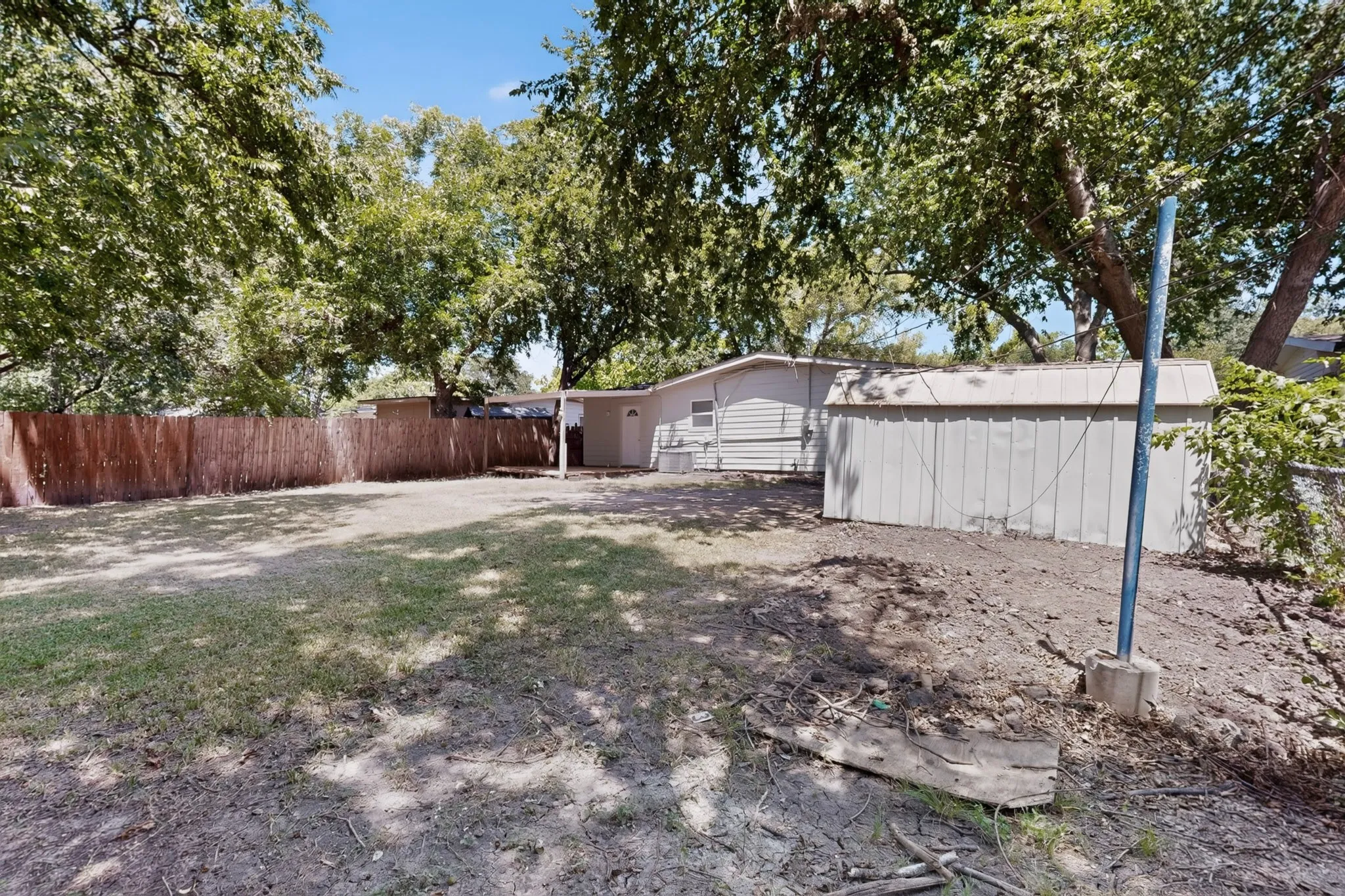 Expansive backyard featuring a partial wooden fence, a detached storage shed with a metal roof, and numerous mature trees providing natural canopy