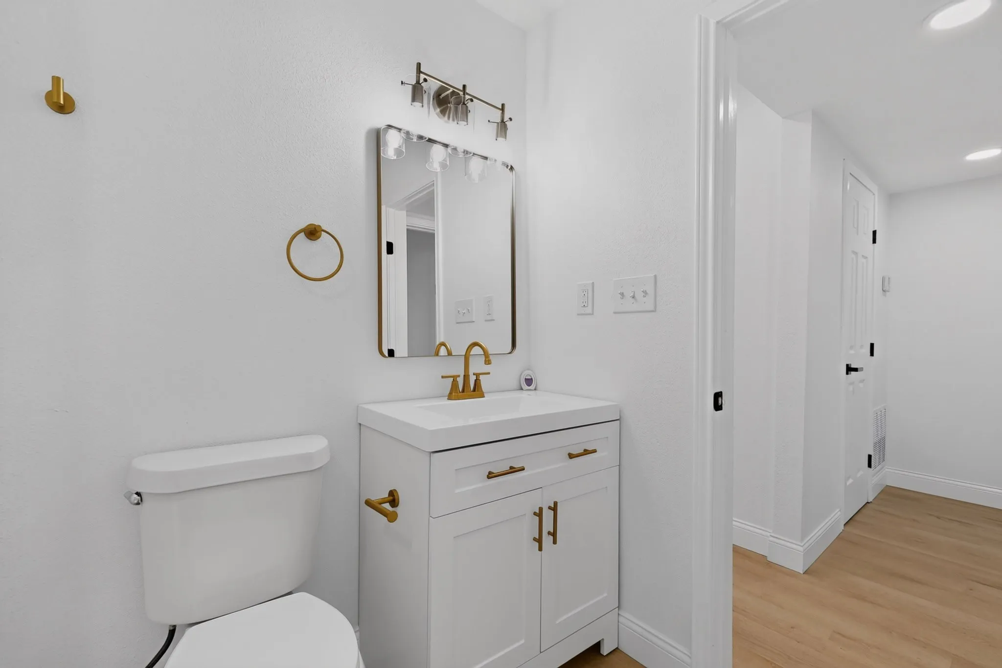 Modern bathroom featuring a white vanity with integrated sink, gold-tone fixtures, framed mirror, and recessed lighting