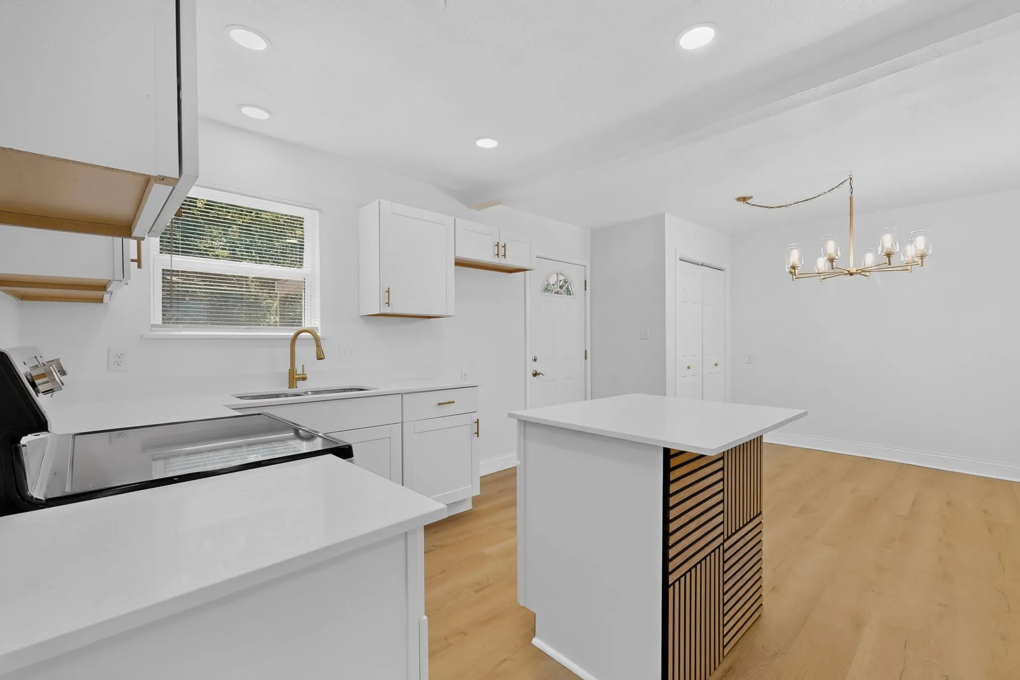 Modern kitchen area featuring white cabinetry, light-toned wood-finish flooring, and a central island with a contrasting wood slat design