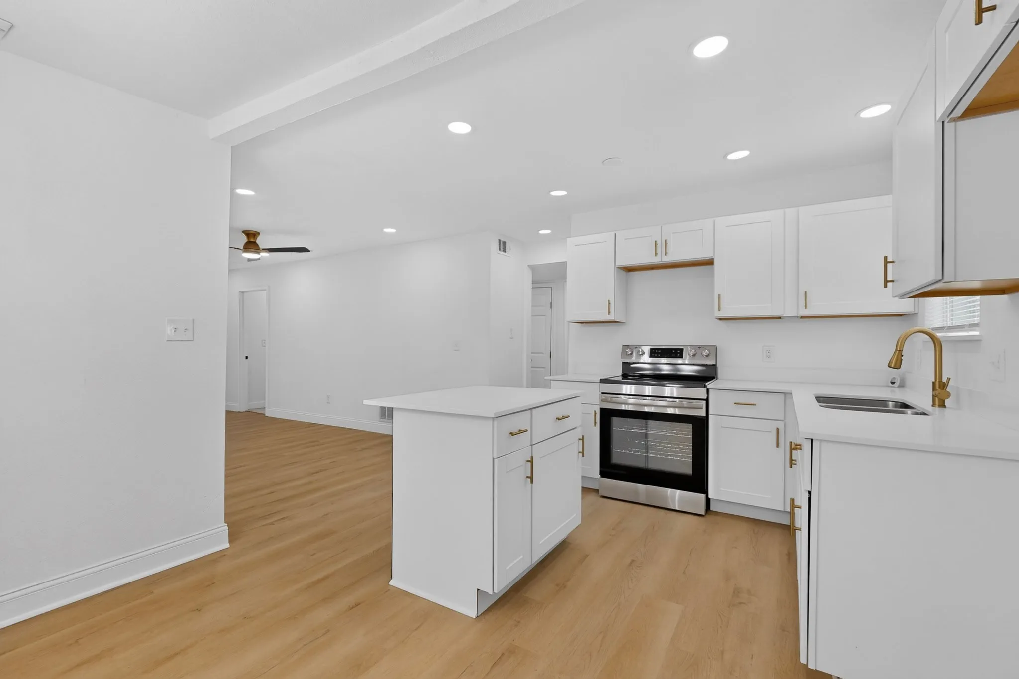 Modern kitchen featuring white cabinetry with gold-tone hardware, stainless steel appliances, a single-basin sink with a gold-tone faucet, and a freestanding island with a countertop