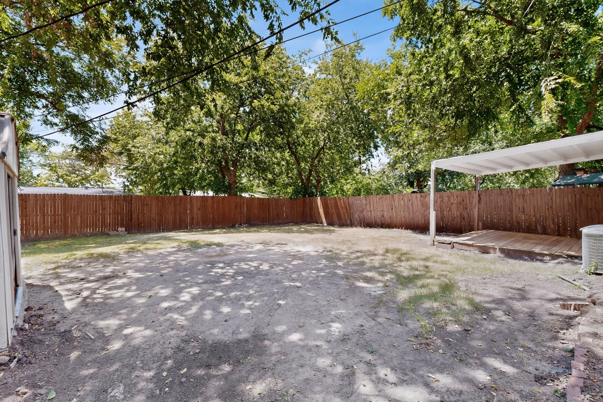 Spacious backyard featuring a wooden privacy fence, a covered deck, and mature trees