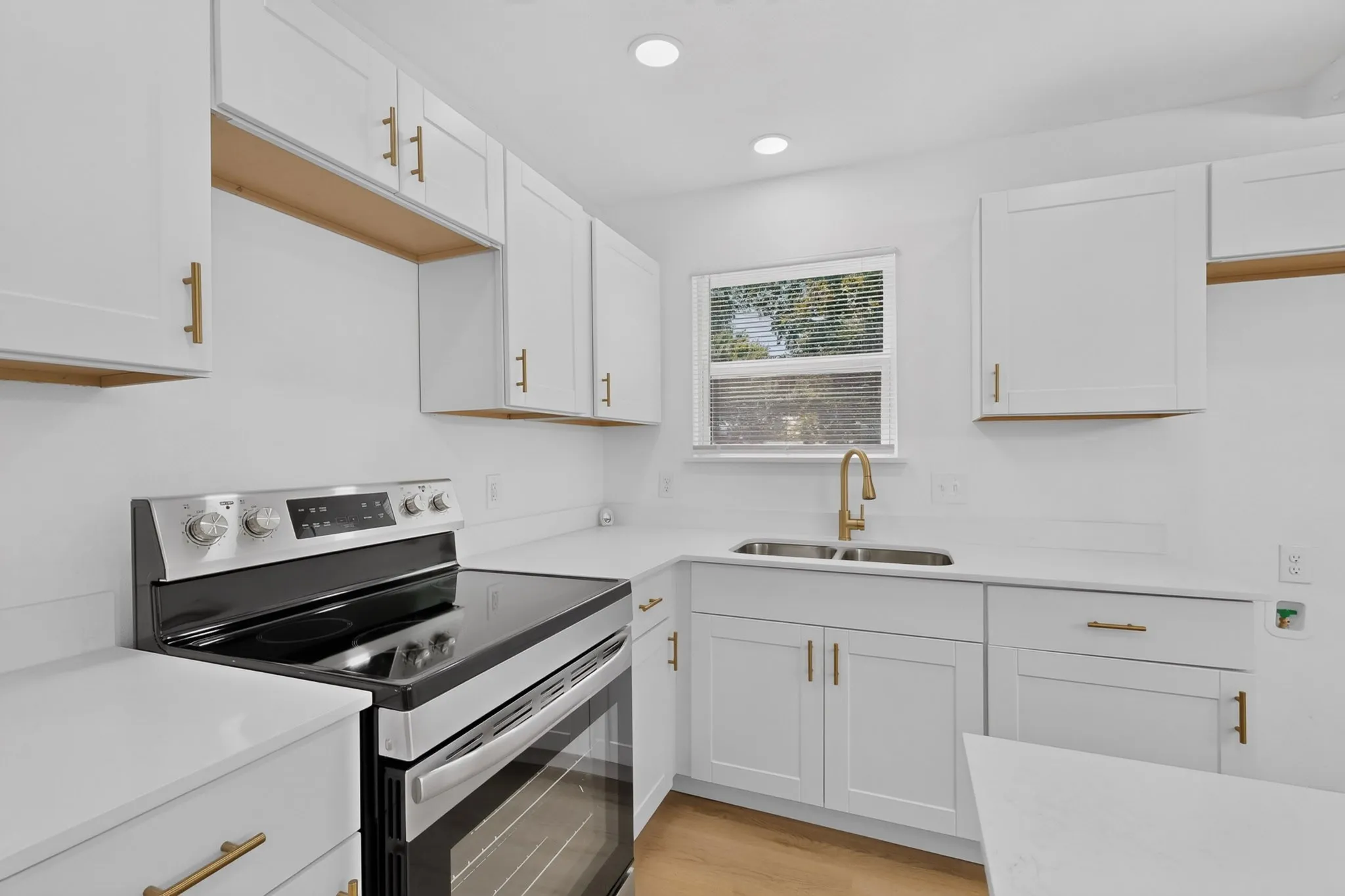 Modern kitchen featuring white shaker cabinetry with gold-tone hardware, white countertops, and a stainless steel electric range