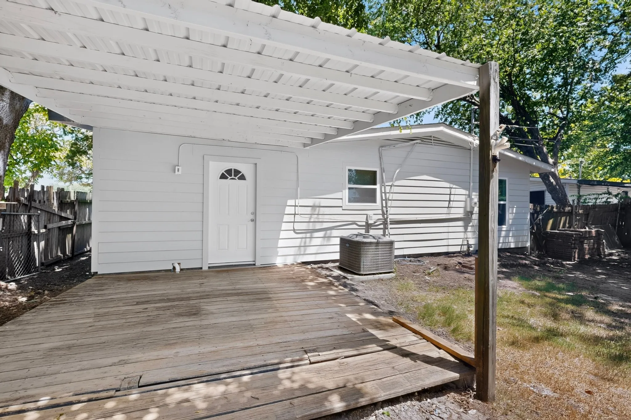 Covered wood-plank patio with exterior door, white siding, and outdoor utility unit