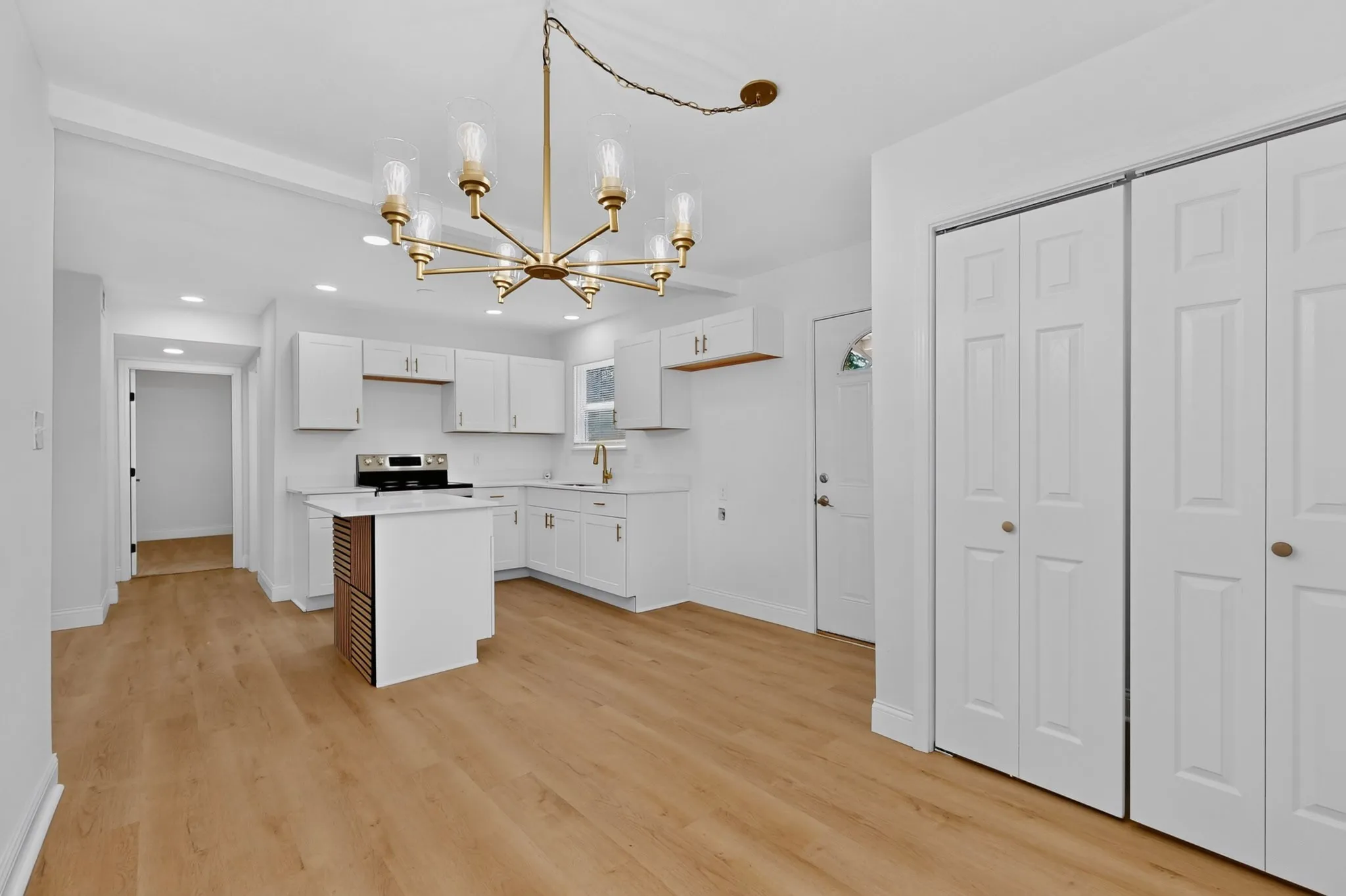 Open concept kitchen and dining area featuring a modern chandelier, wood-finish flooring, white cabinetry, a kitchen island with accent paneling, and bi-fold closet doors