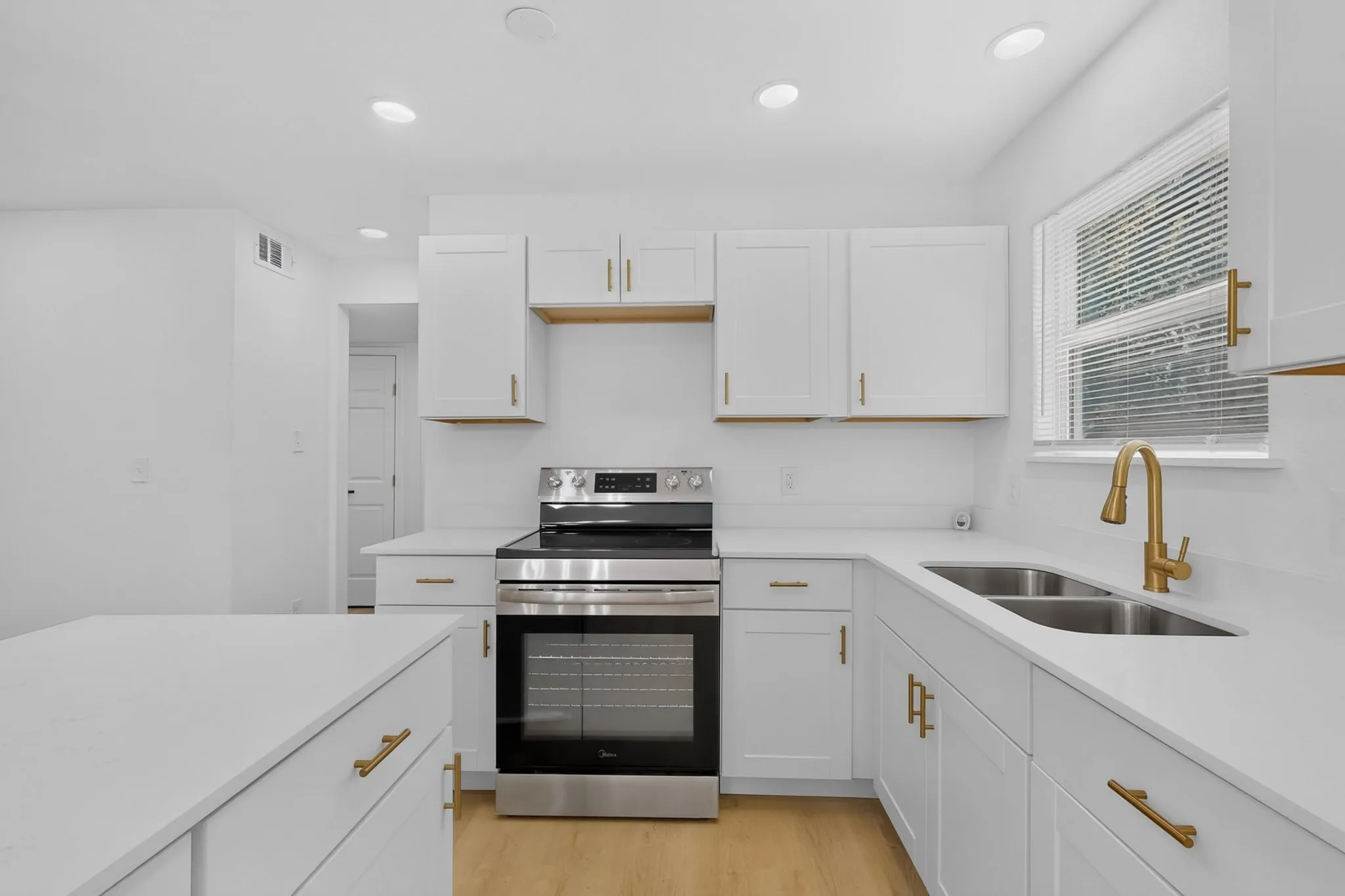 Contemporary kitchen featuring white cabinetry with gold-tone hardware, stainless steel appliances, and light wood-finish flooring