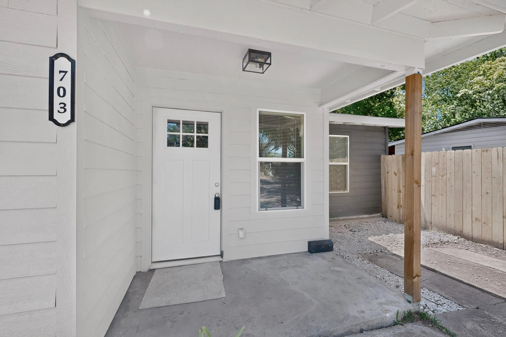 Covered front entry featuring a white paneled door with glass inserts, wood-finish siding, and a contemporary exterior light fixture