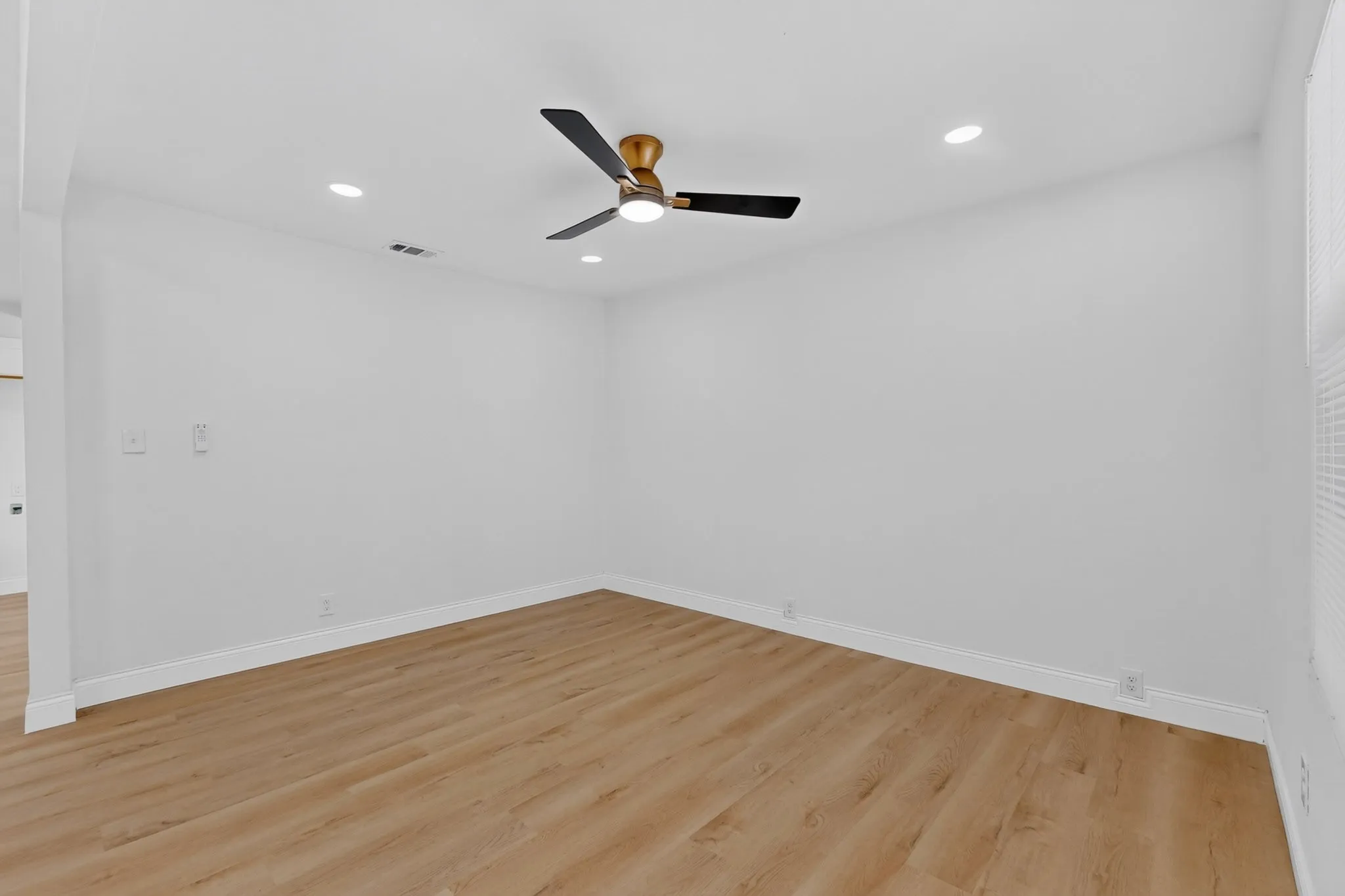 Spacious room featuring light wood-finish flooring, recessed lighting, a modern ceiling fan with a bronze-tone motor and black blades, white walls, and white baseboards