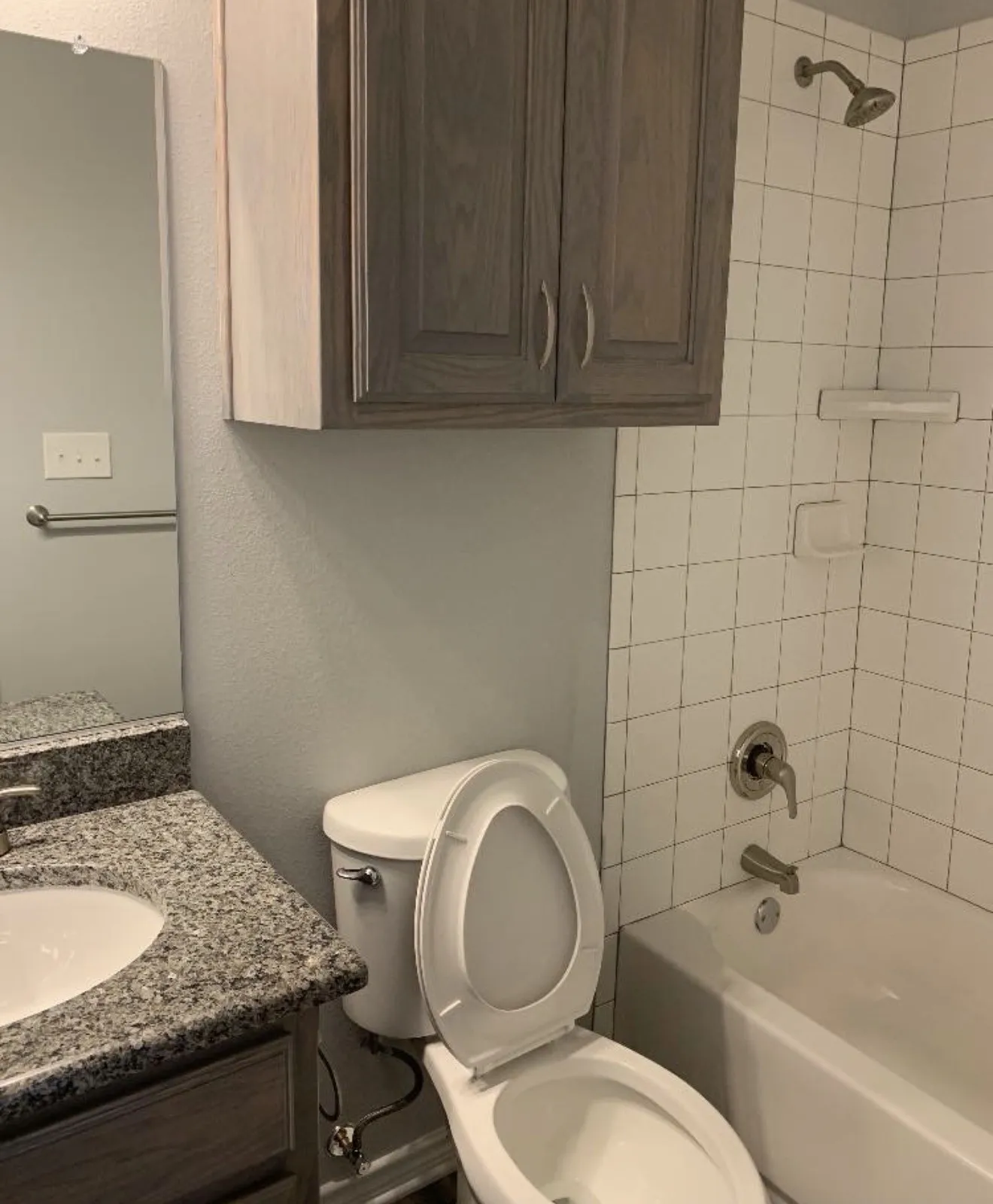 Granite-style countertop with integrated sink, wood-finish vanity, overhead wood-finish cabinetry, and tiled shower with tub
